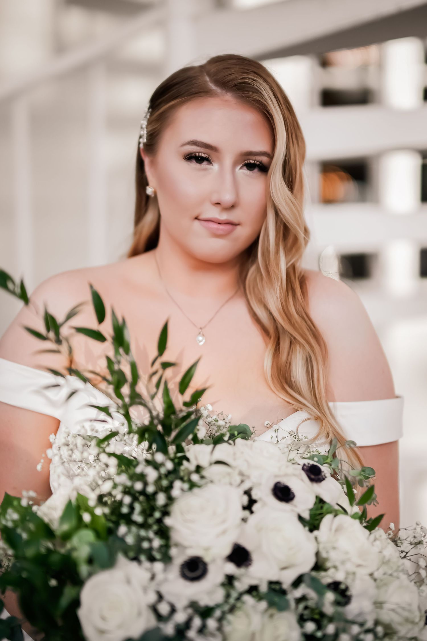 Bride holding stunning white and black anemone bouquet with greenery.