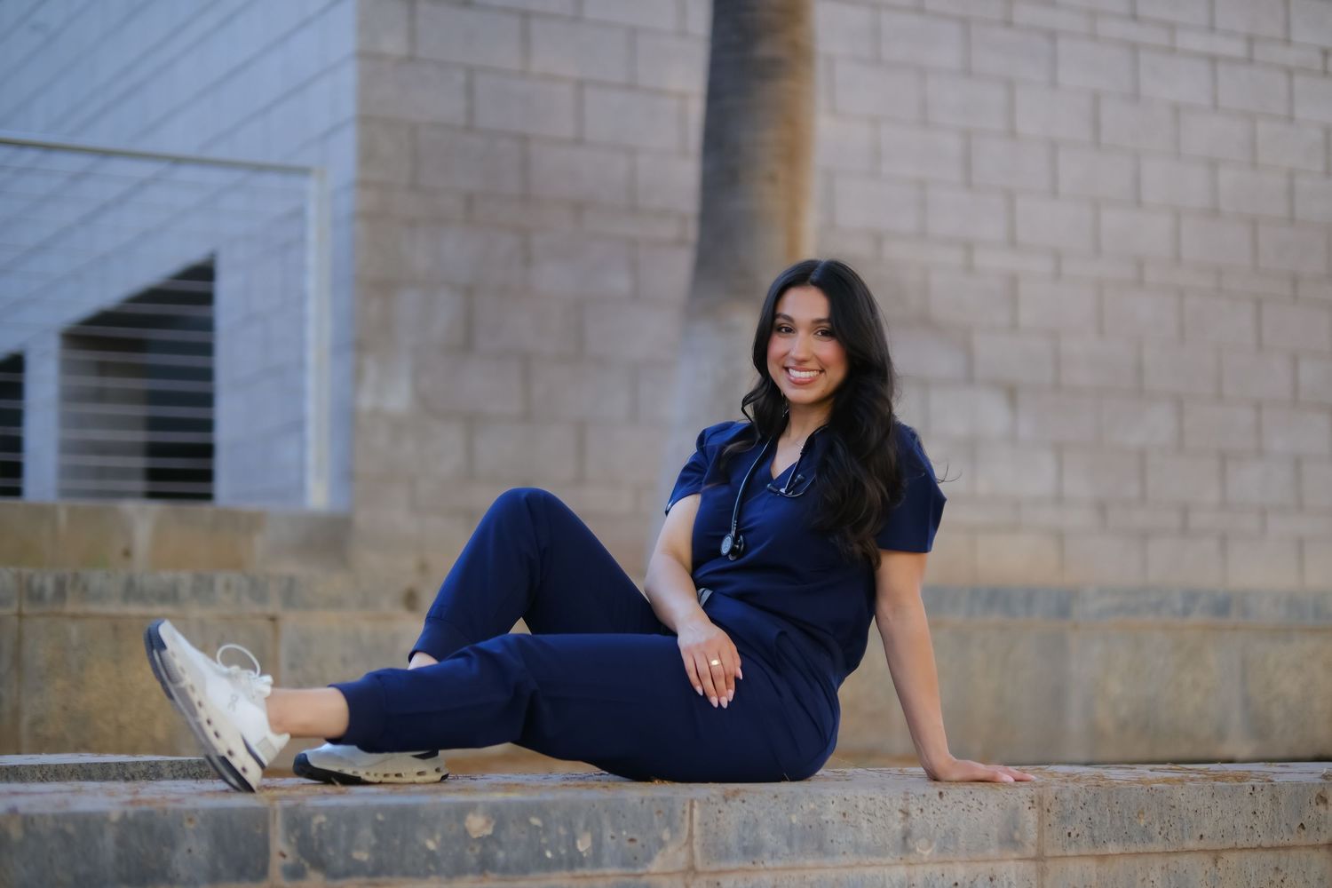 Person in navy blue jumpsuit sitting casually on concrete steps while wearing white sneakers.