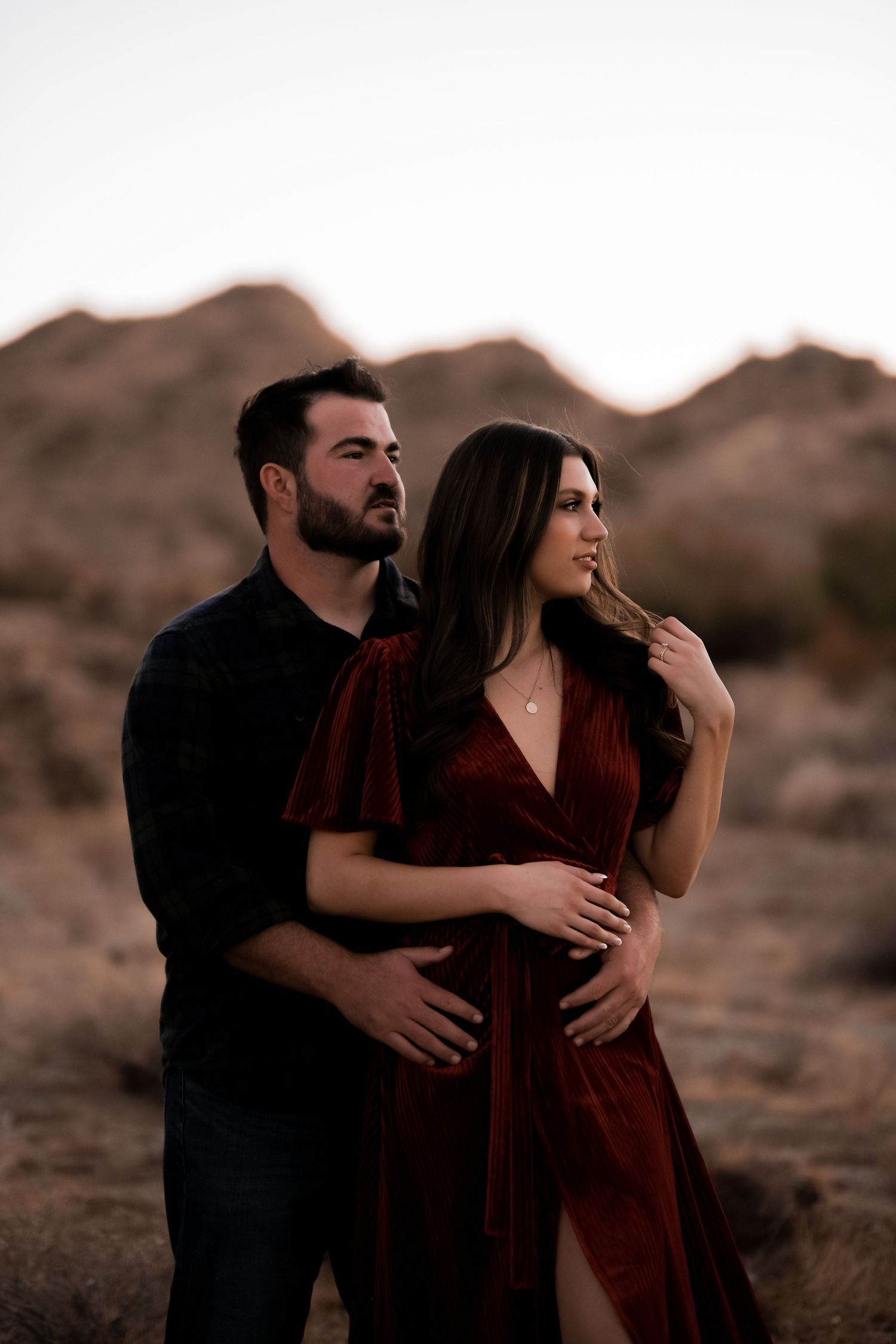 Couple in desert landscape at sunset with mountains in background.