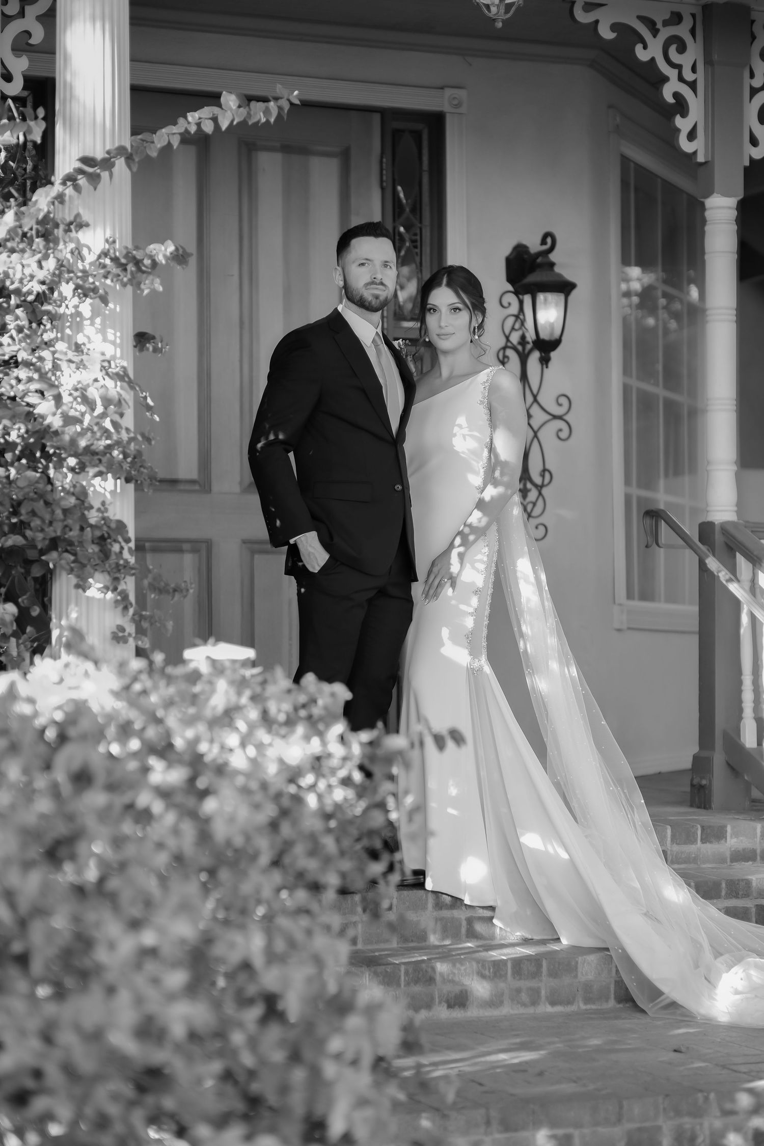 Elegant black and white portrait of newlyweds standing on brick steps with vintage architectural details.