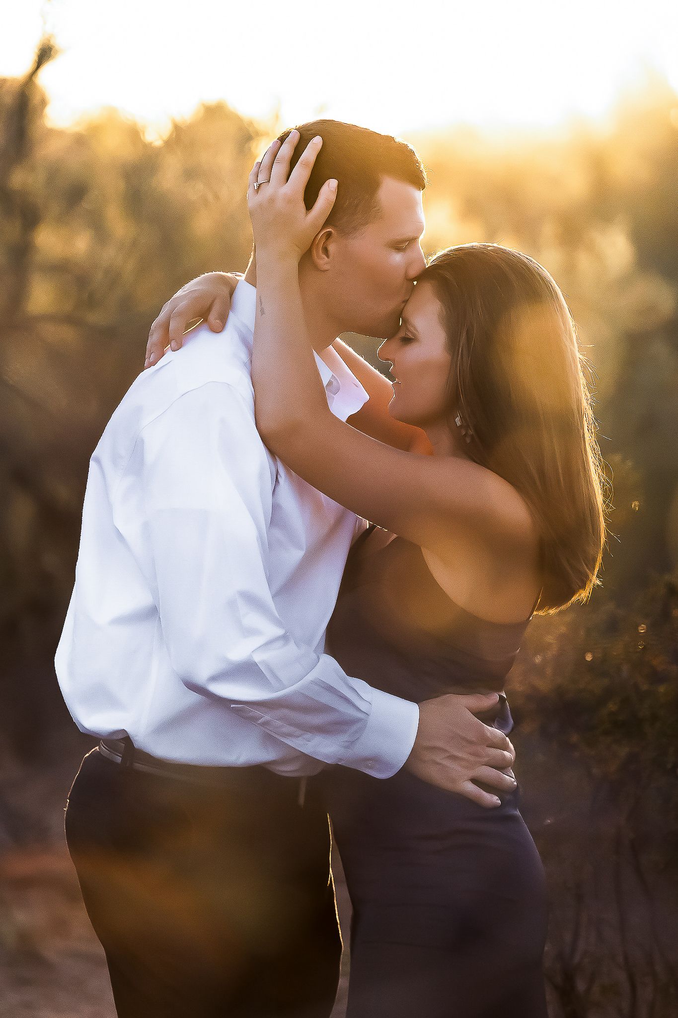 A romantic couple embraces in golden sunset light while sharing an intimate moment outdoors.