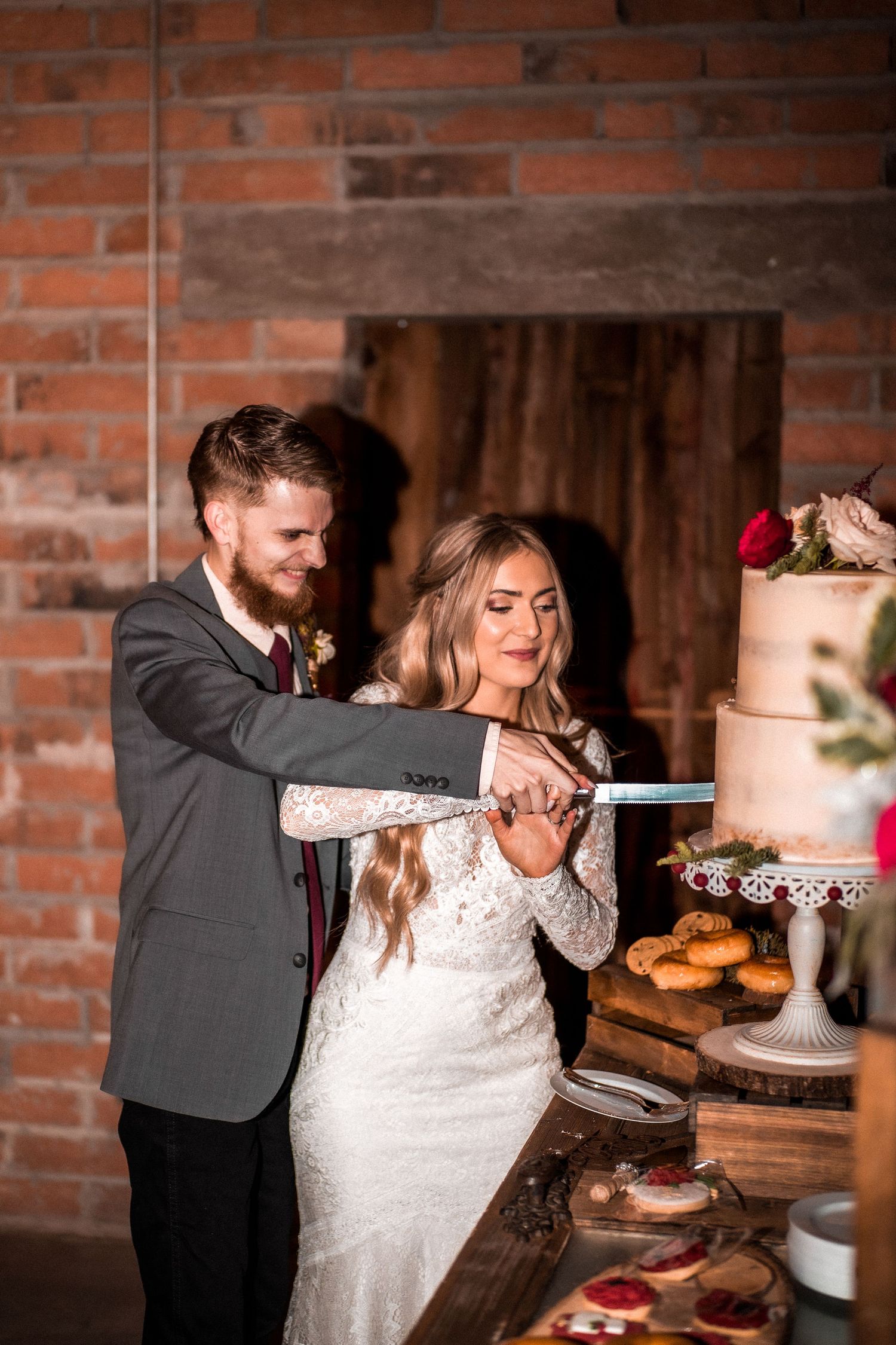 Bride and groom cut their wedding cake together in a rustic brick-walled venue.