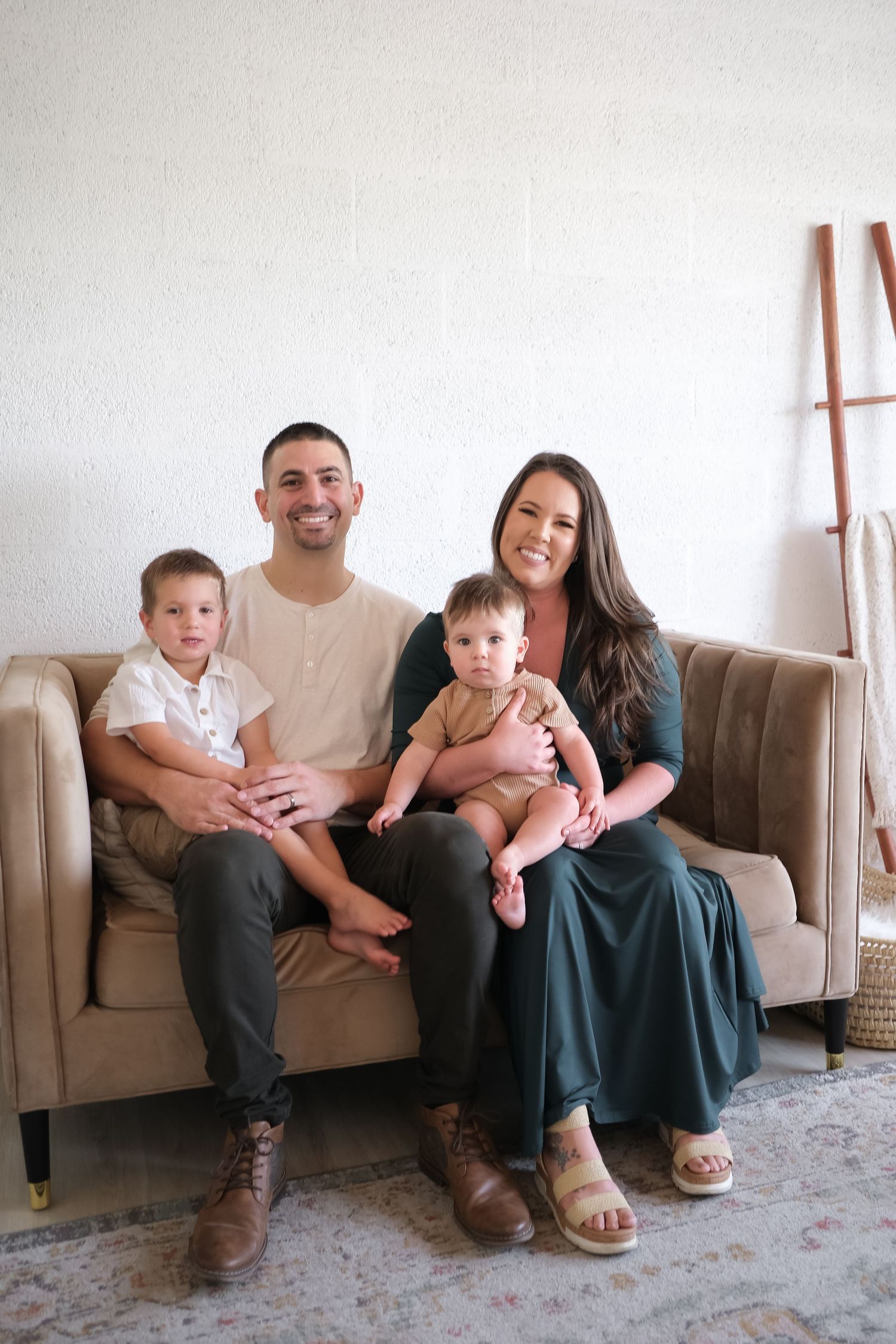 A family relaxes together on a tan couch in a minimalist living room with white walls.