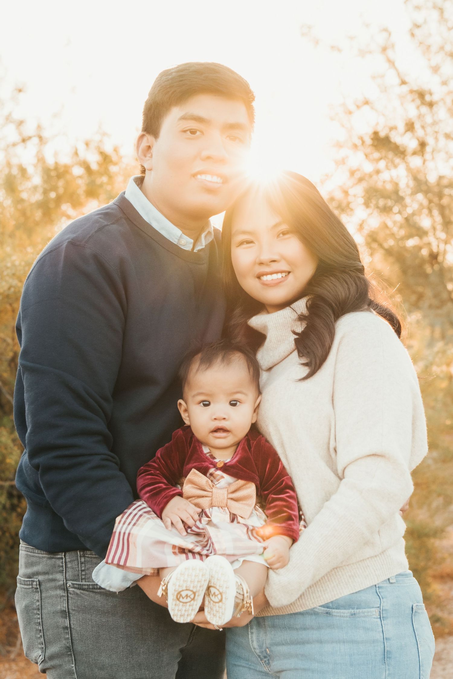 Family of three poses together in warm sweaters during golden hour portrait session.