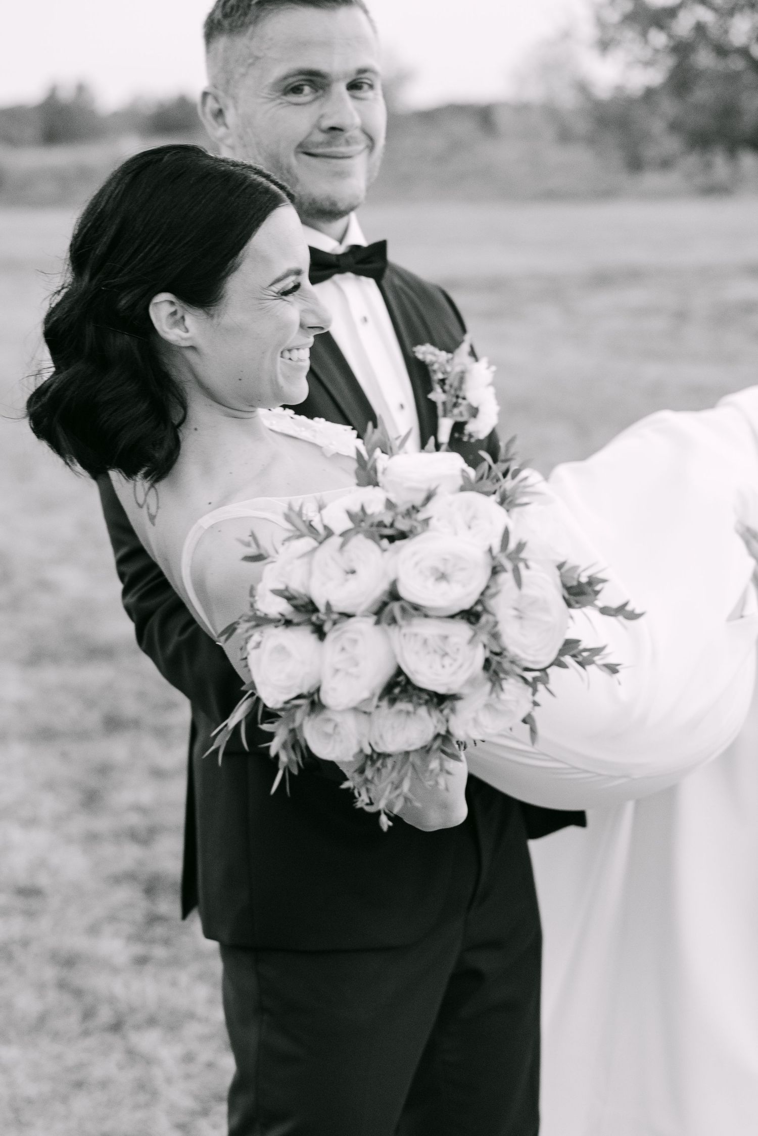 A black and white wedding photo showing a couple embracing outdoors with a beautiful bouquet of roses.