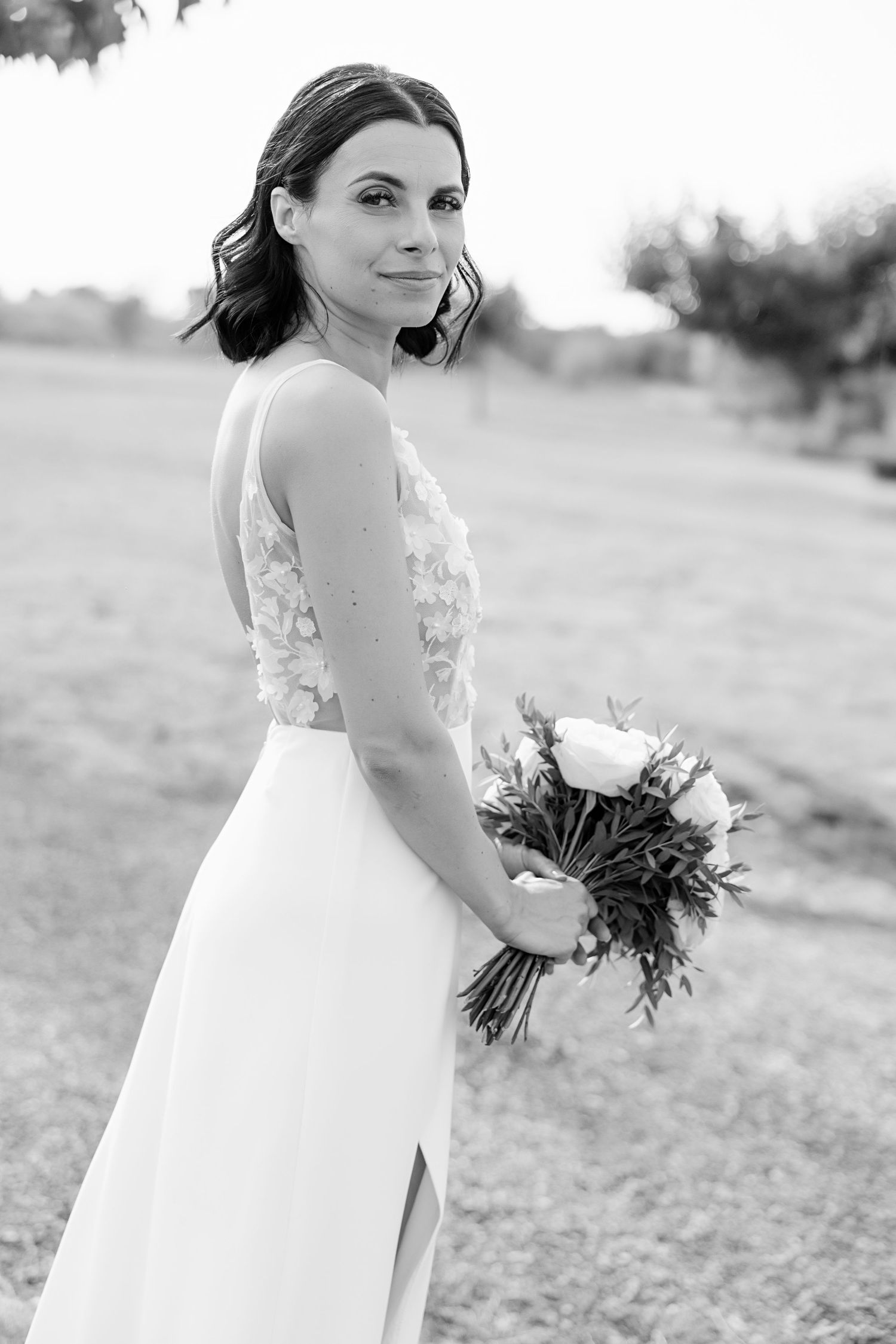 Black and white bridal portrait sequence showing bride holding bouquet in lace wedding dress while turning in field.