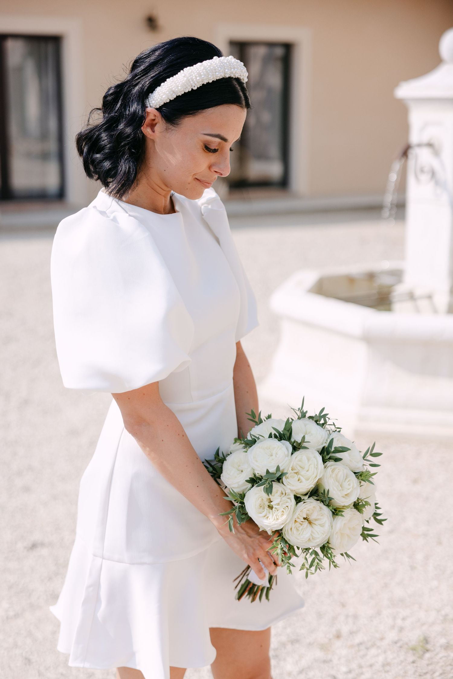 Side profile of a bride in an elegant white dress with puff sleeves holding a delicate white and green bouquet outdoors.
