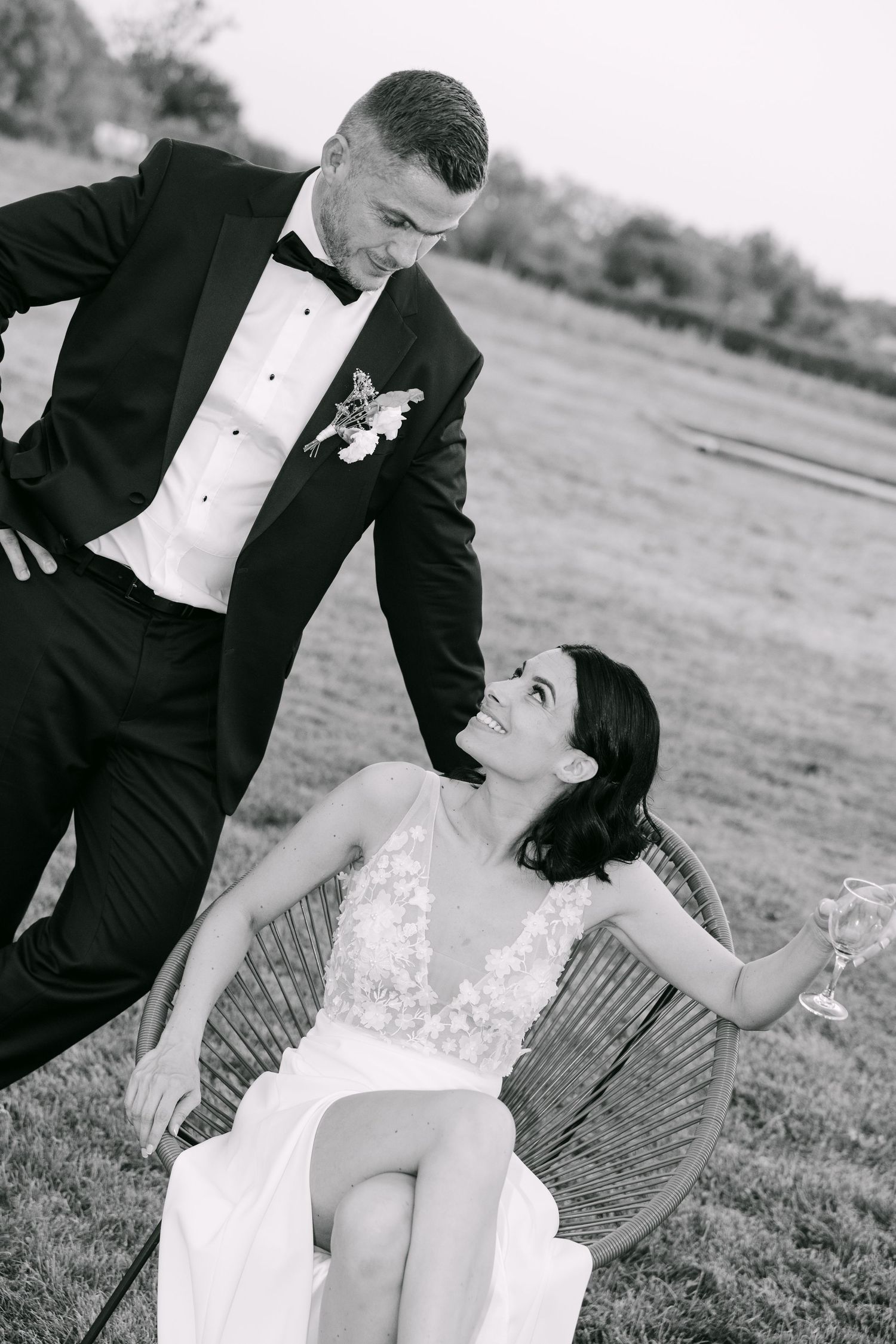 A romantic black and white photo sequence of a couple in formal wedding attire having a playful moment in a field.