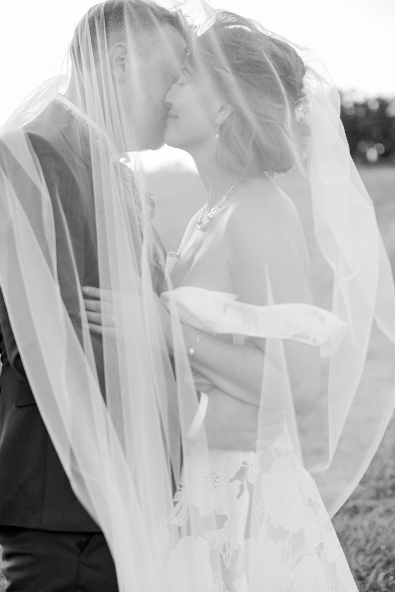 Black and white photo of couple kissing under billowing wedding veil.