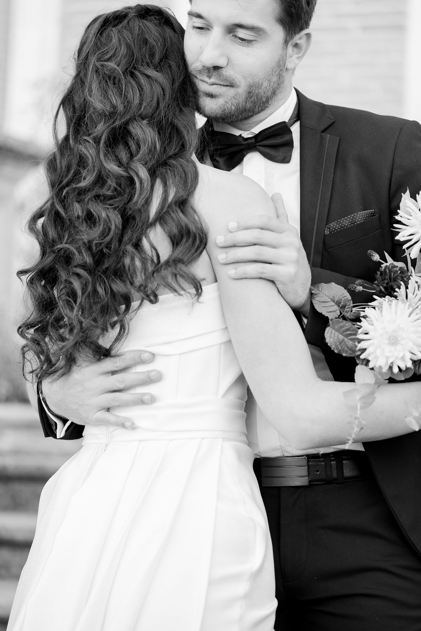 Black and white photograph of a romantic wedding embrace showing curly hair and a bowtie.