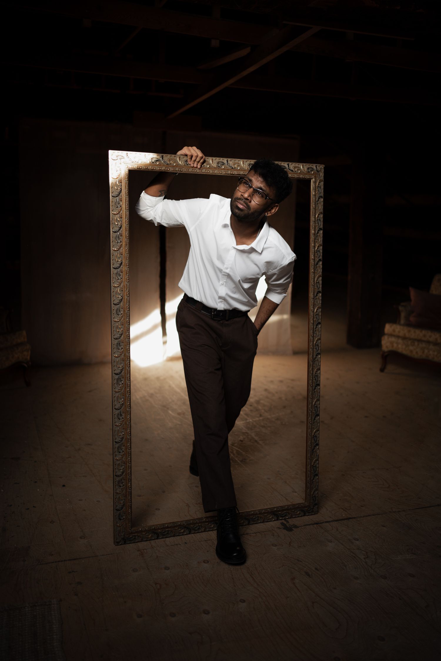 Artistic portrait through an ornate frame showing a figure in white shirt and dark pants.