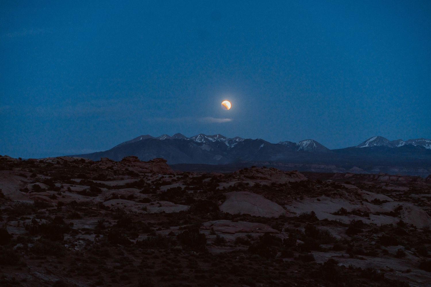 A panoramic view of mountains under a dark blue sky with a crescent moon.
