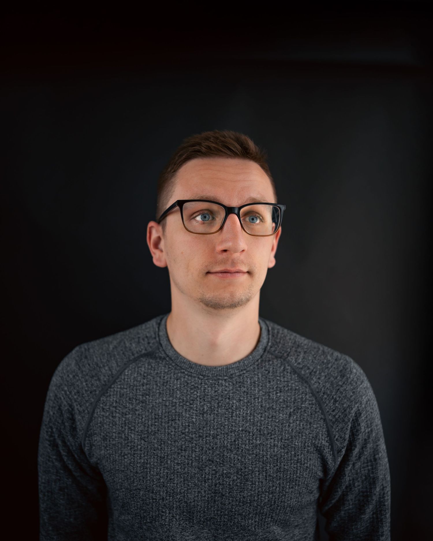 Studio portrait series against dark background wearing grey sweater.