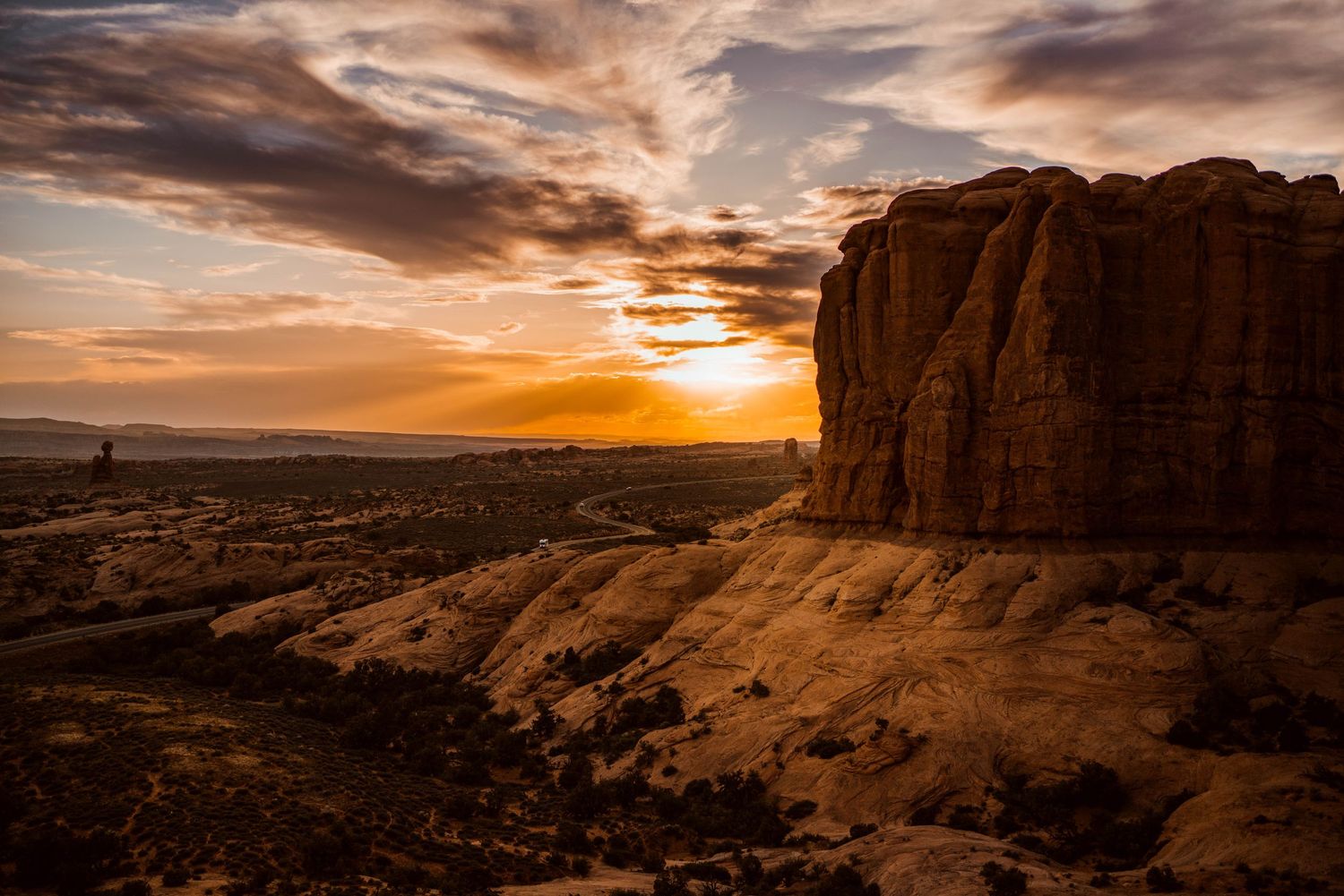 Dramatic desert sunset behind red rock cliffs in Arches National Park.