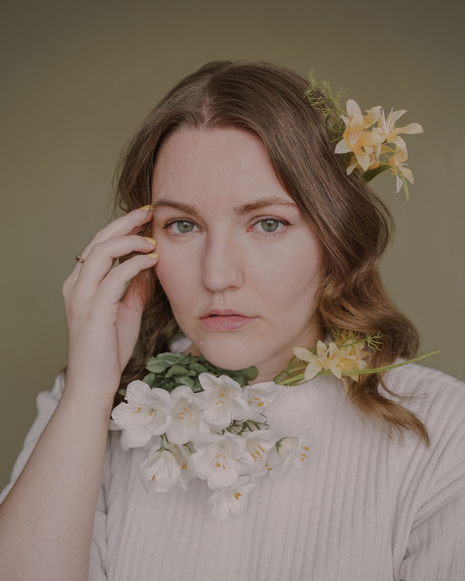 Artistic portrait featuring yellow lilies and a cream sweater against a muted green background.