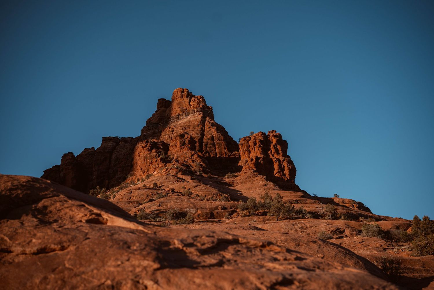 Red rock formations rise against a deep blue sky in a desert landscape.