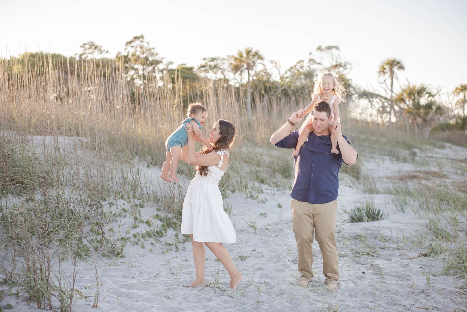 Parents lifting children up high while playing on sandy beach dunes at sunset. Charleston, South Carolina. Salt and Oak Photography.