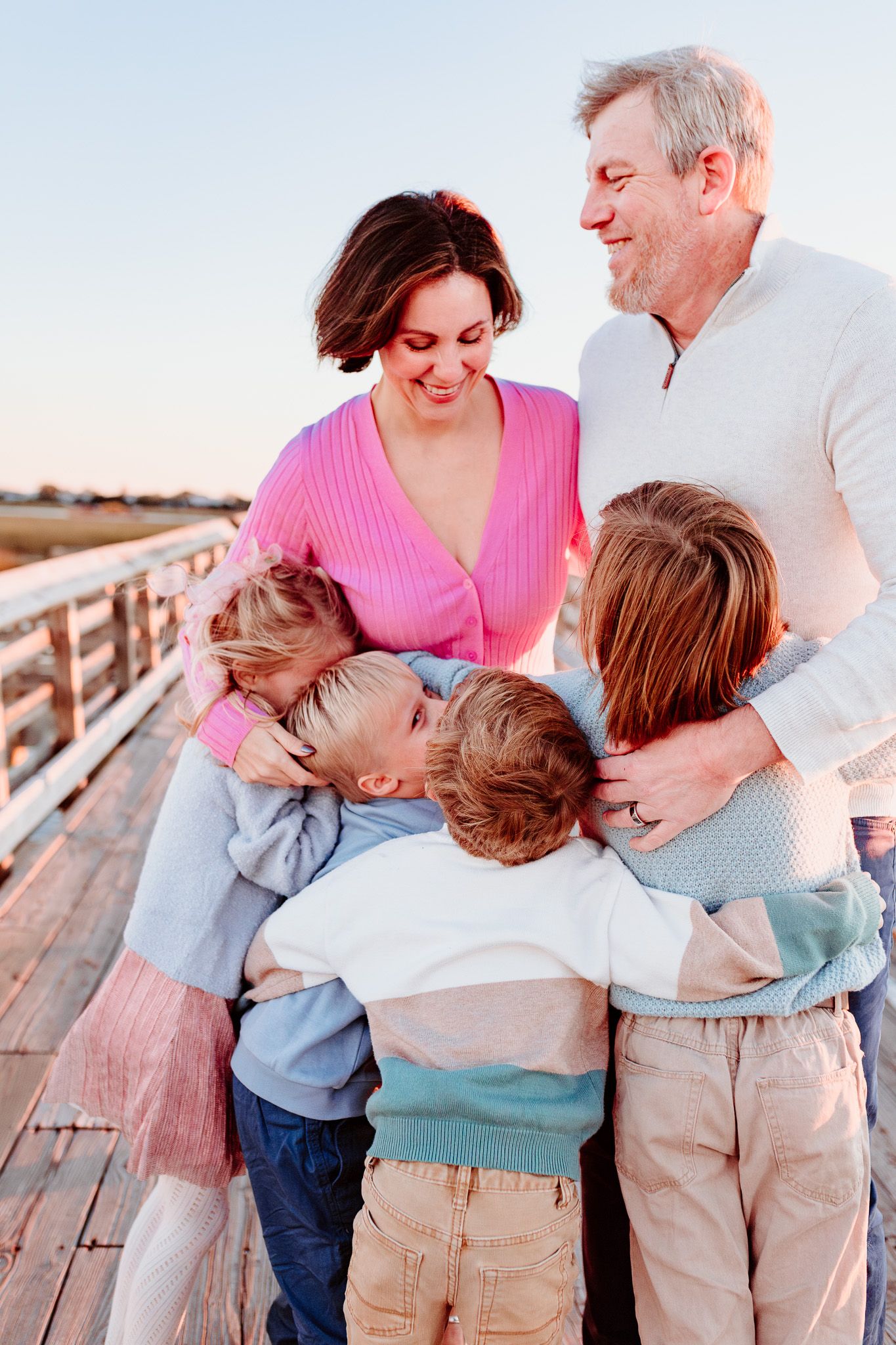 Family shares warm embrace on wooden pier during sunset. Charleston, South Carolina. Salt and Oak Photography.