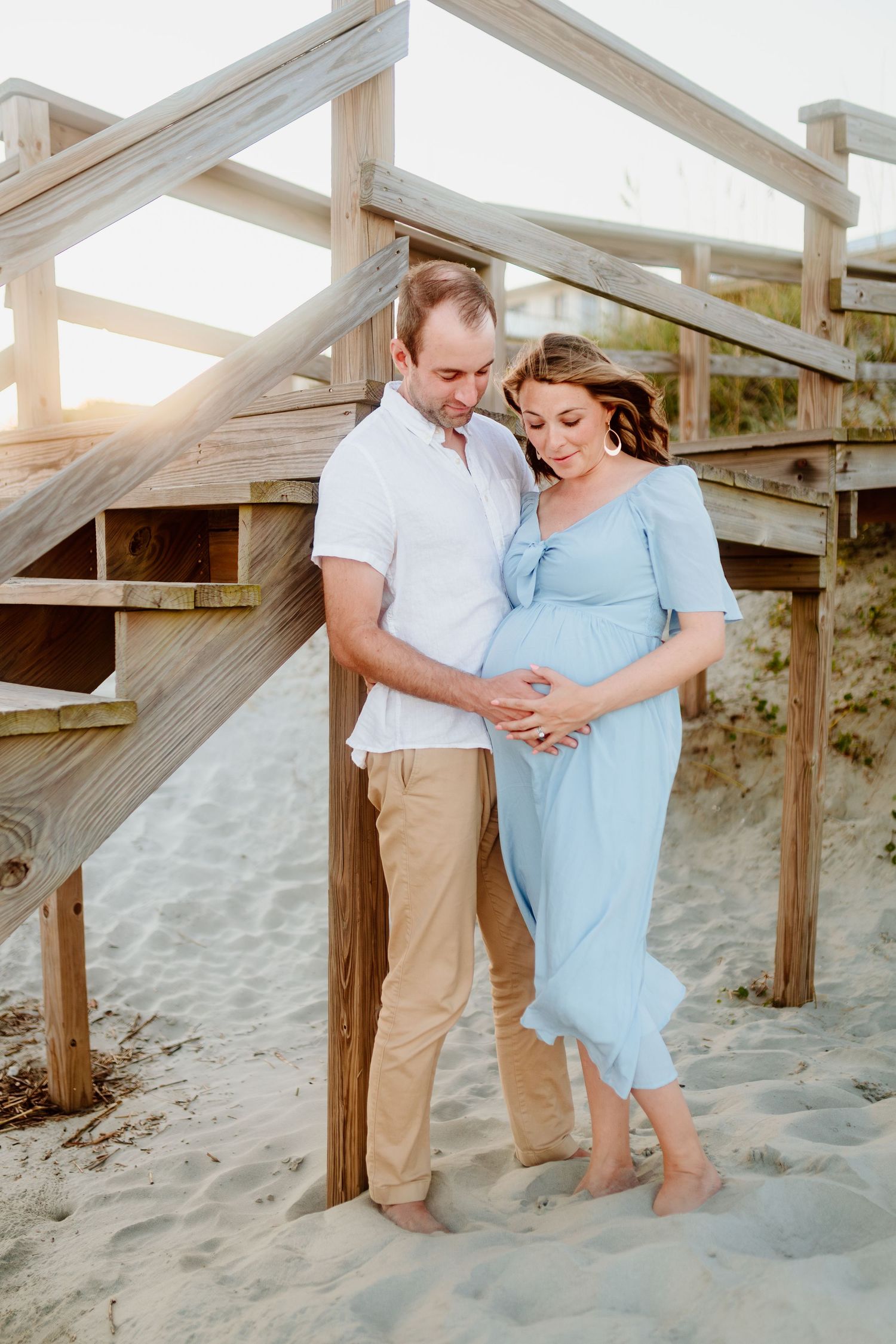 Expectant couple embracing by wooden beach stairs during sunset. Charleston, South Carolina. Salt and Oak Photography.