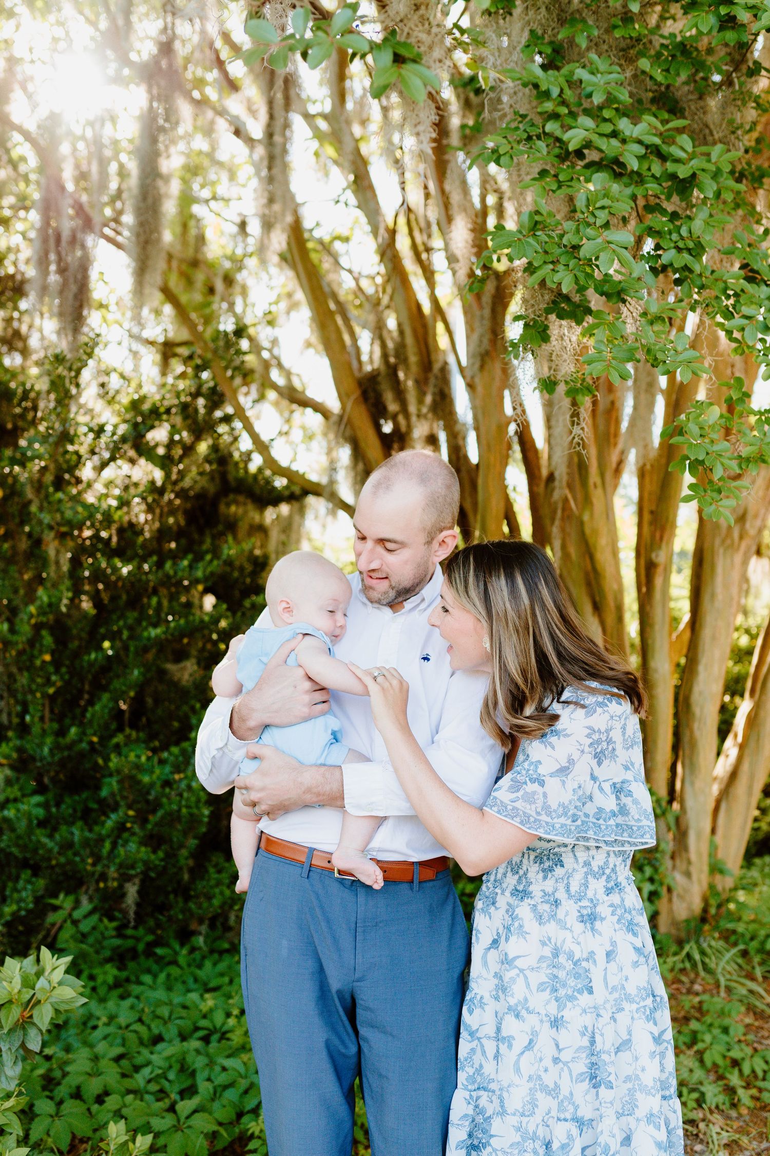 A family shares a tender moment together under sunlit trees in a garden setting. Charleston, South Carolina. Salt and Oak Photography.