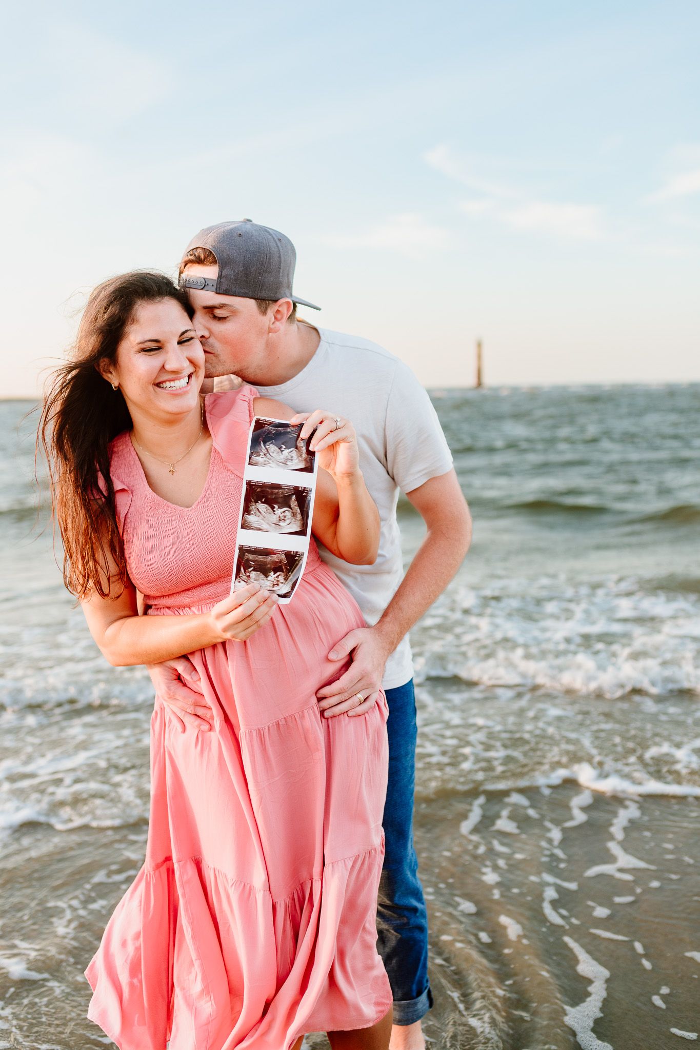Couple shares intimate moment on beach while holding ultrasound photos. Charleston, South Carolina. Salt and Oak Photography.