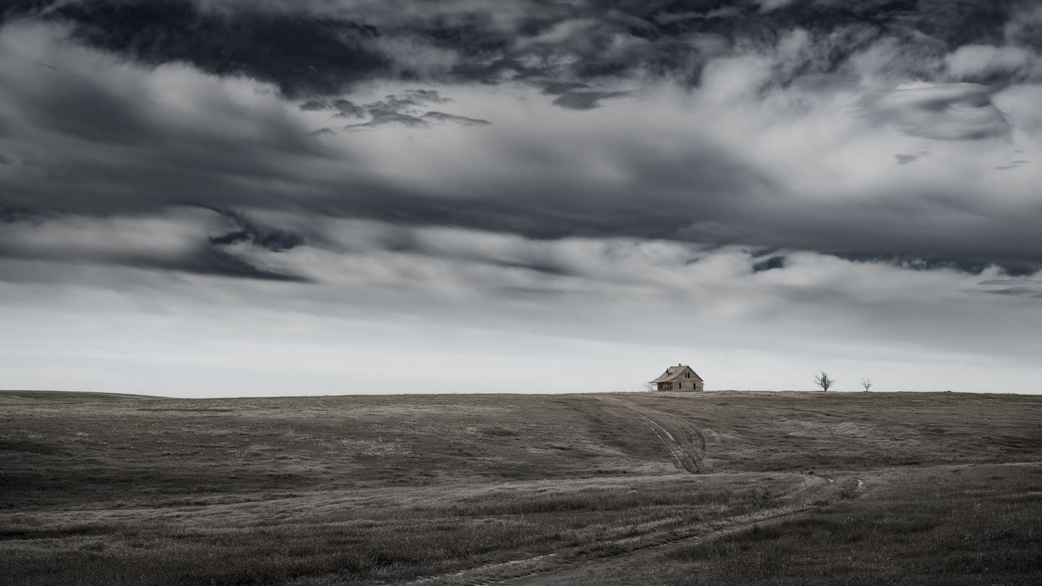 Lone farmhouse on vast barren plains under dramatic stormy sky.