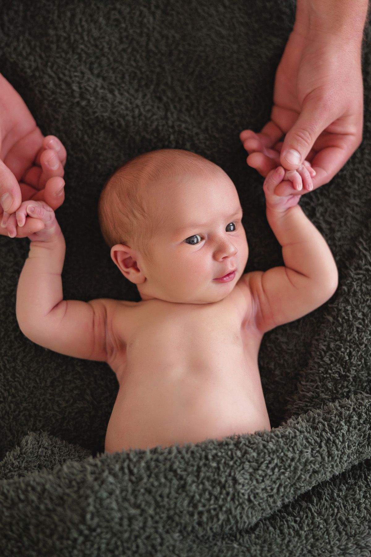 Close-up portrait of newborn baby lying on dark textured blanket.