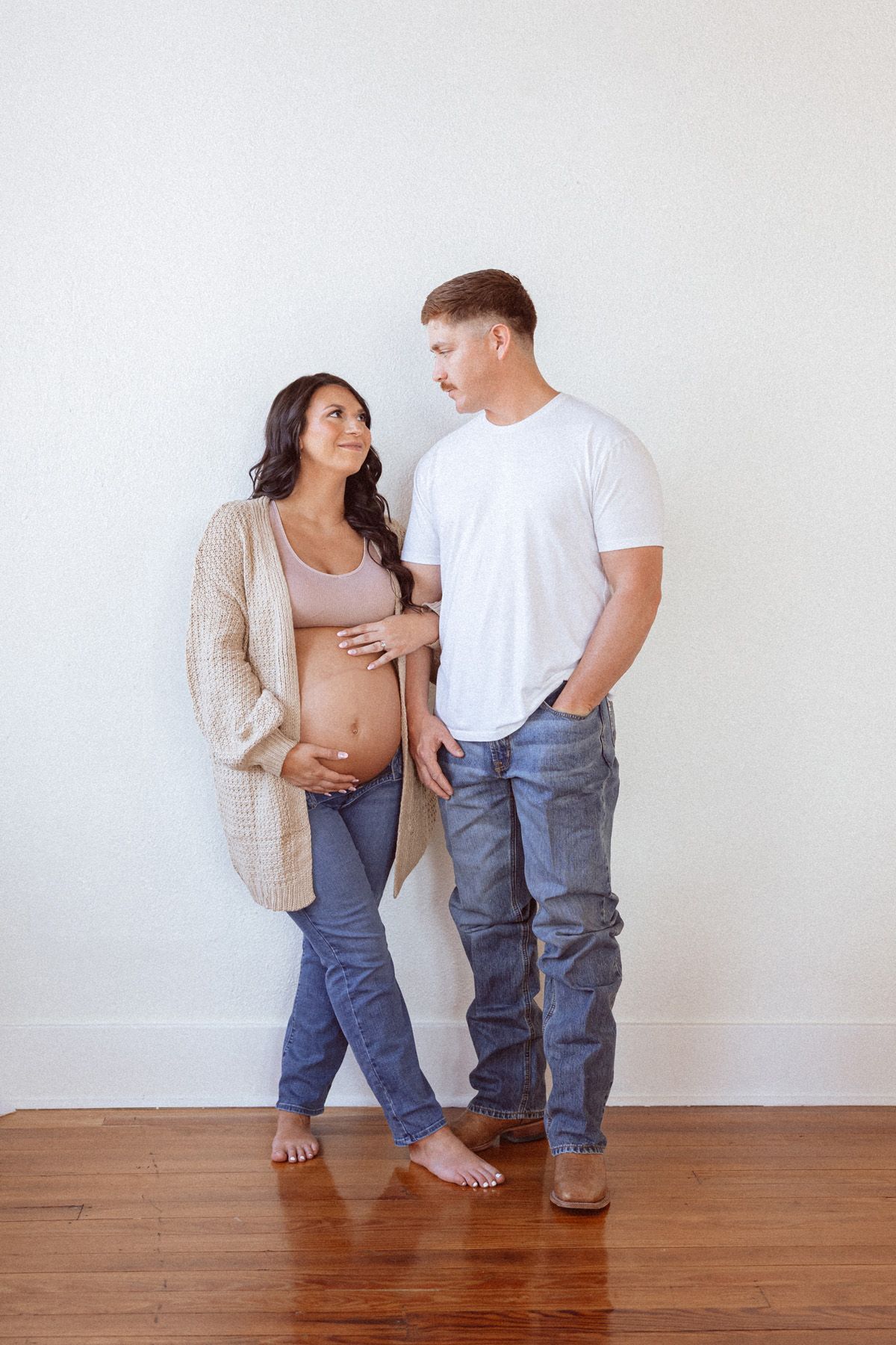 Artistic maternity photos showing couple's legs and embrace on hardwood floor.