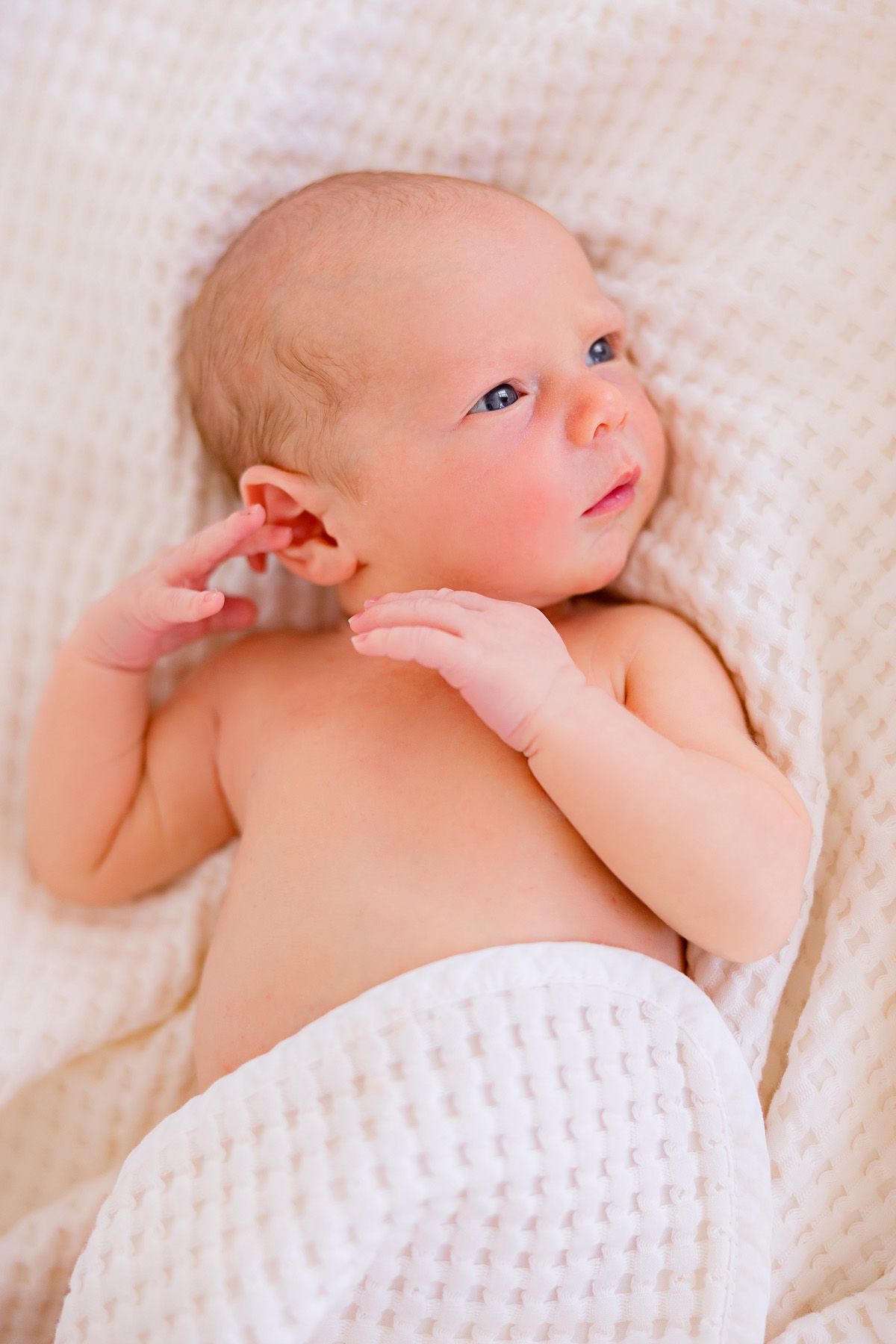 Newborn baby lying on white textured blanket during professional photo session.