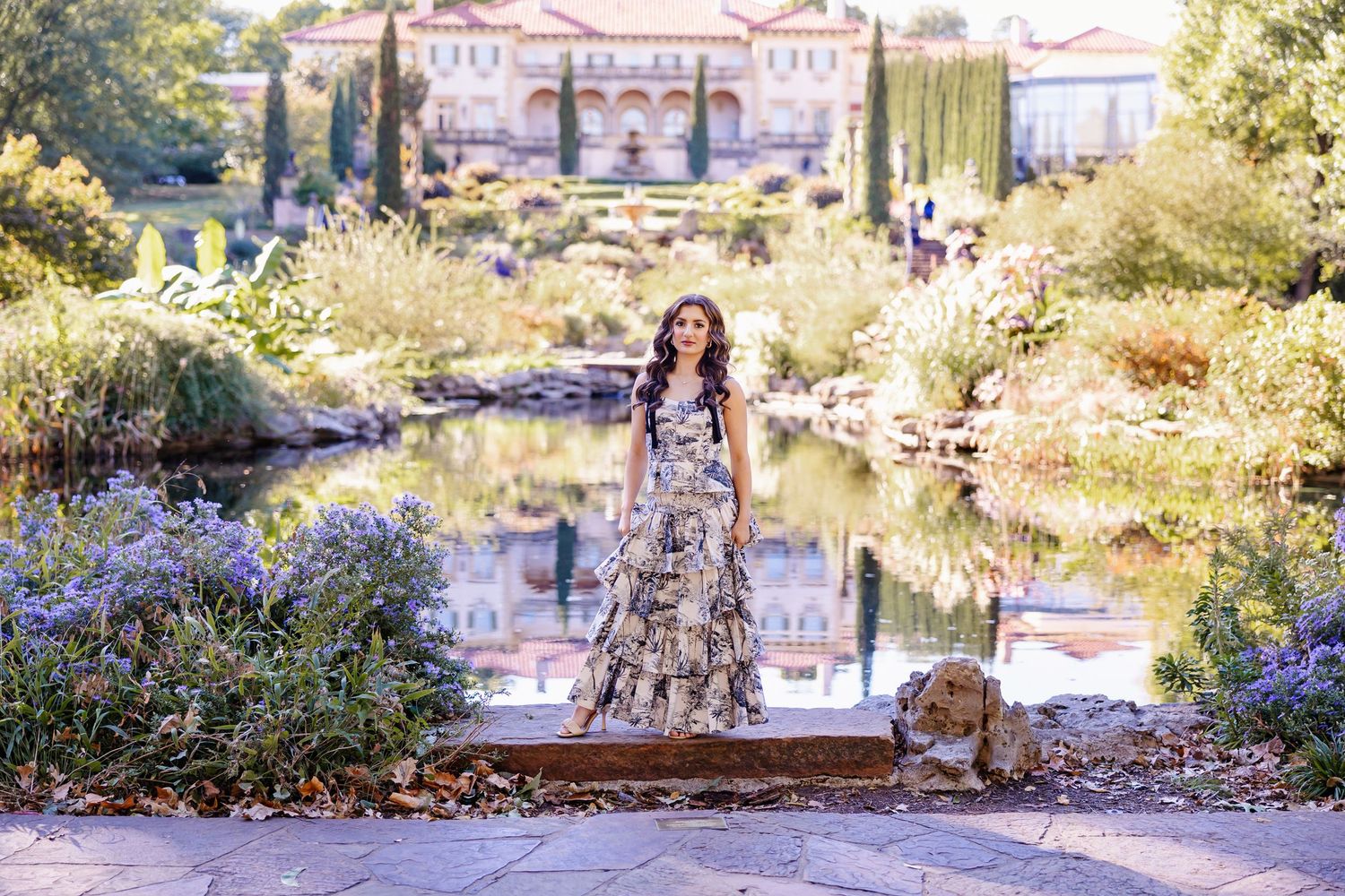 high school senior in flowing dress standing near reflecting pool in the Philbrook Gardens