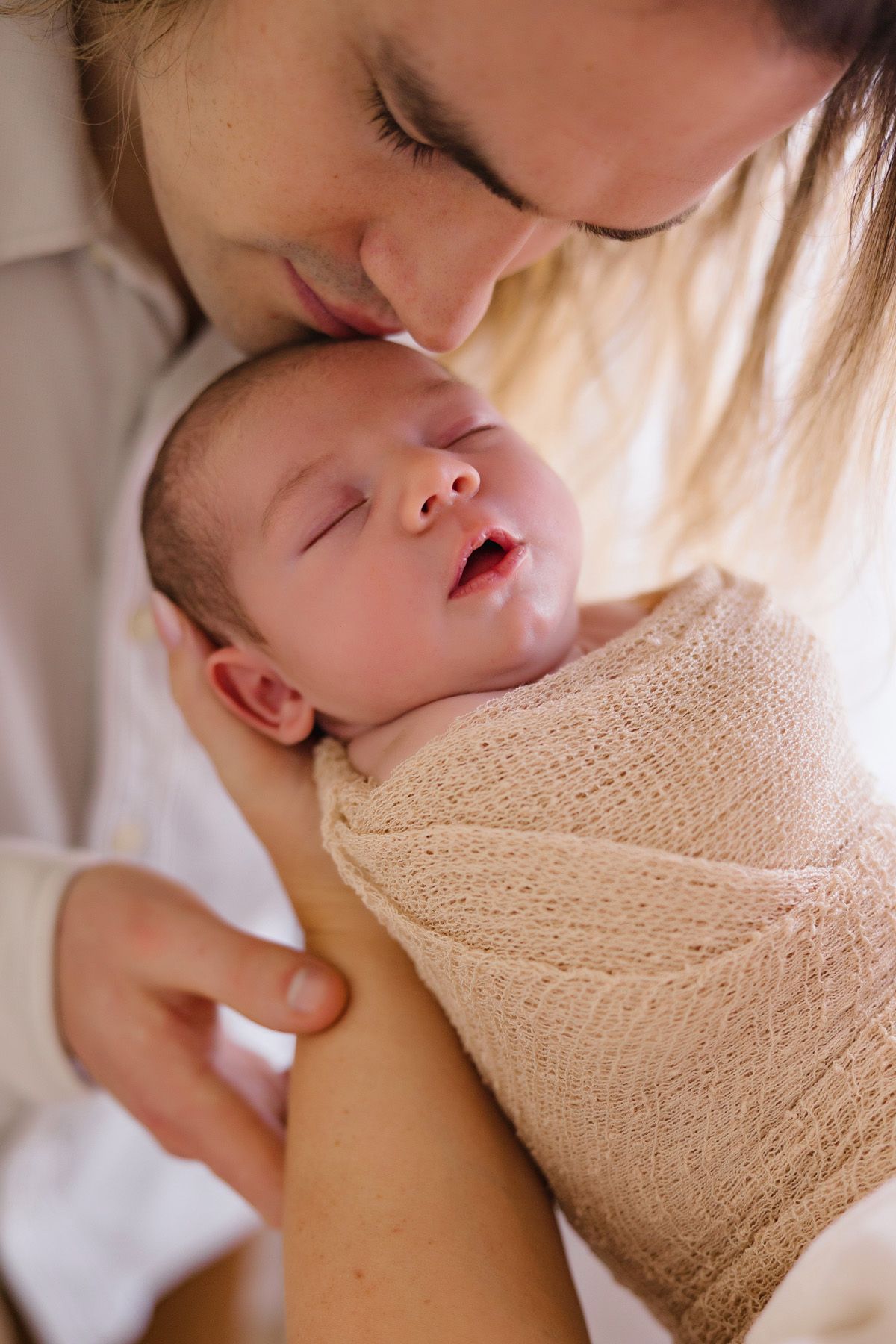 Close-up shots of a newborn baby being cradled in soft beige blankets.
