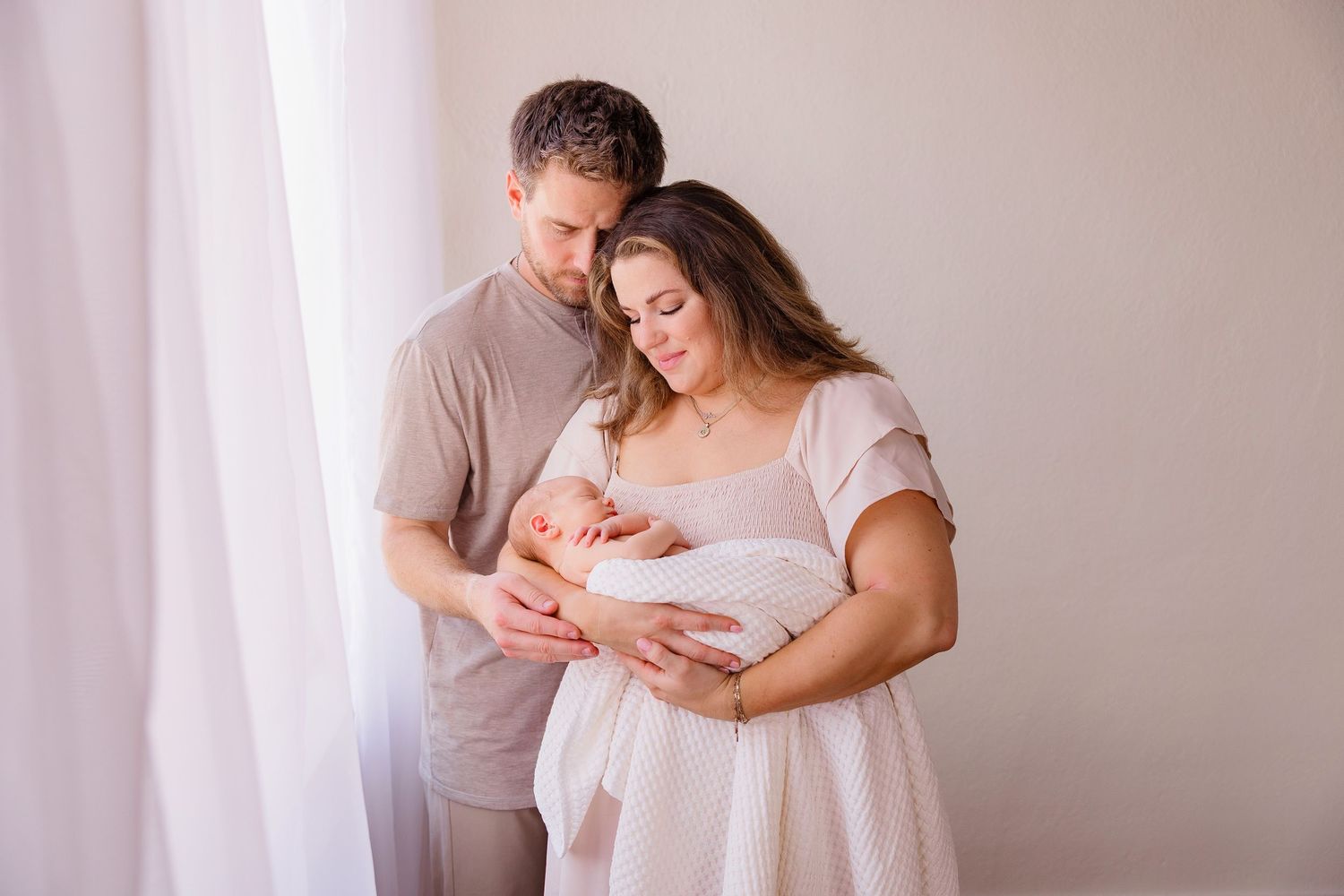 Lifestyle newborn photography session with parents in a bright minimalist setting.