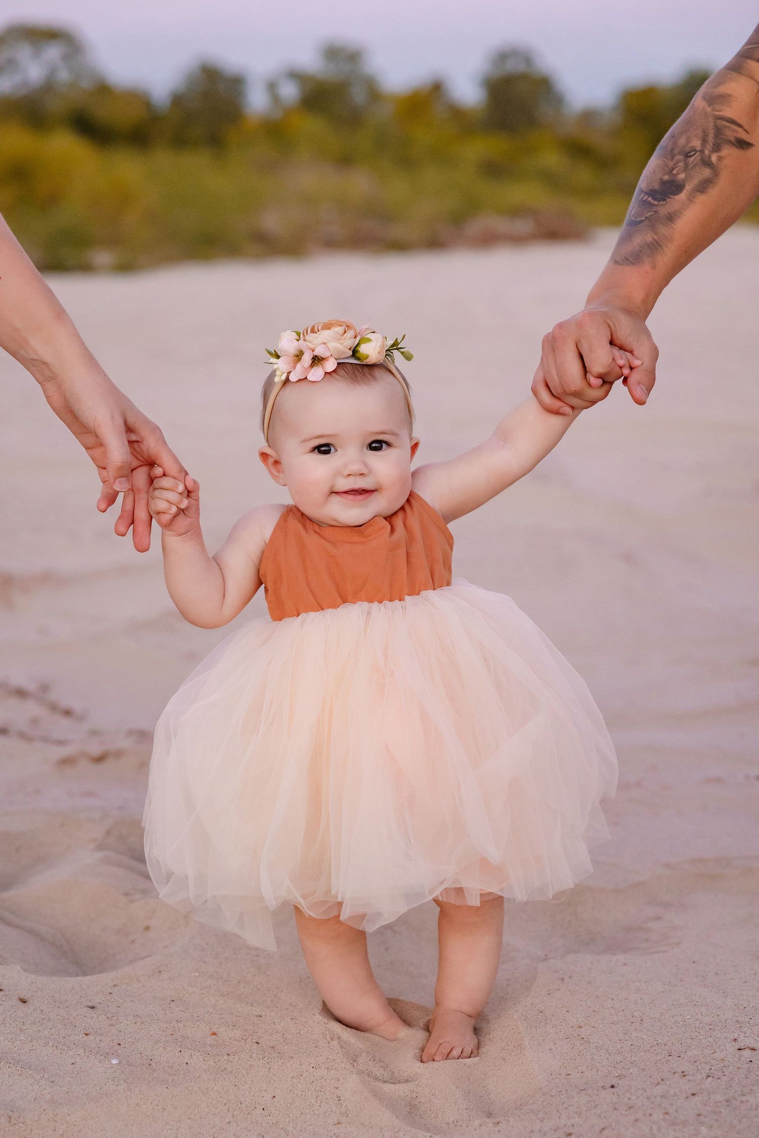 Baby pictures in a peach tutu dress take first steps on sandy ground during sunset beach setting