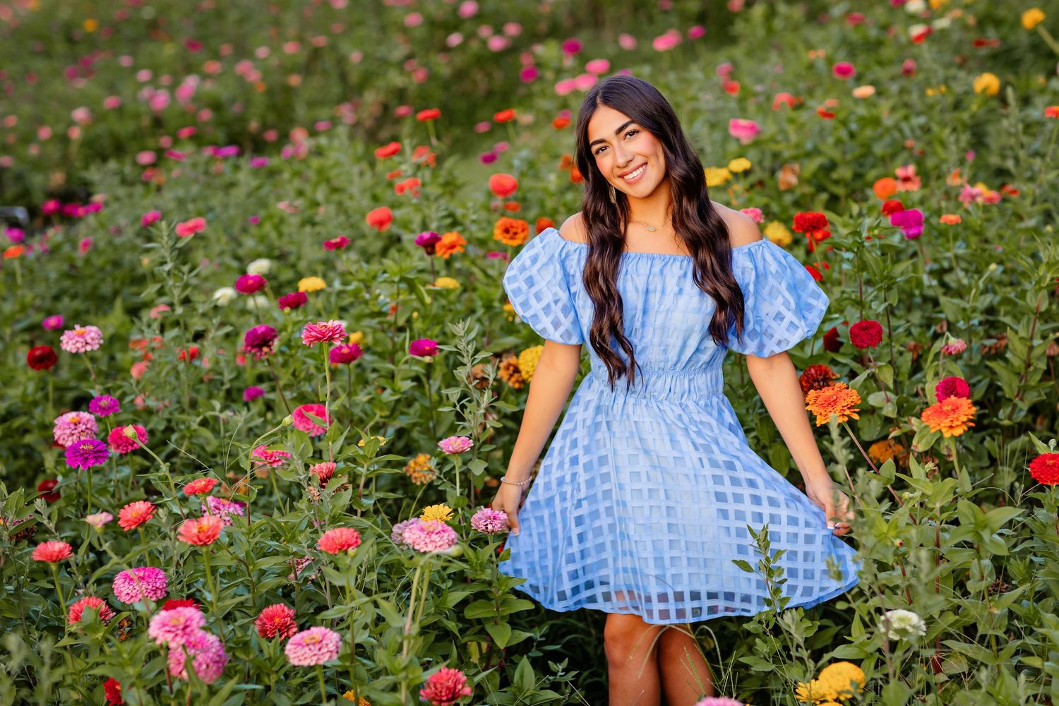 senior girl in blue lace dress standing among colorful garden flowers zennias on sunny day at Sunny Acres Farm