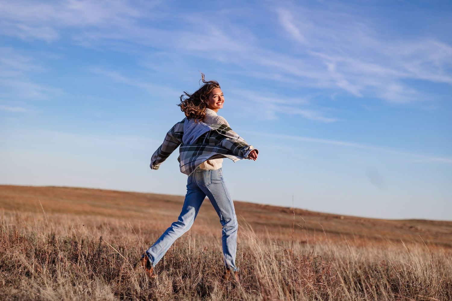 senior girl in denim running freely through golden prairie field under blue sky Wichita mountains