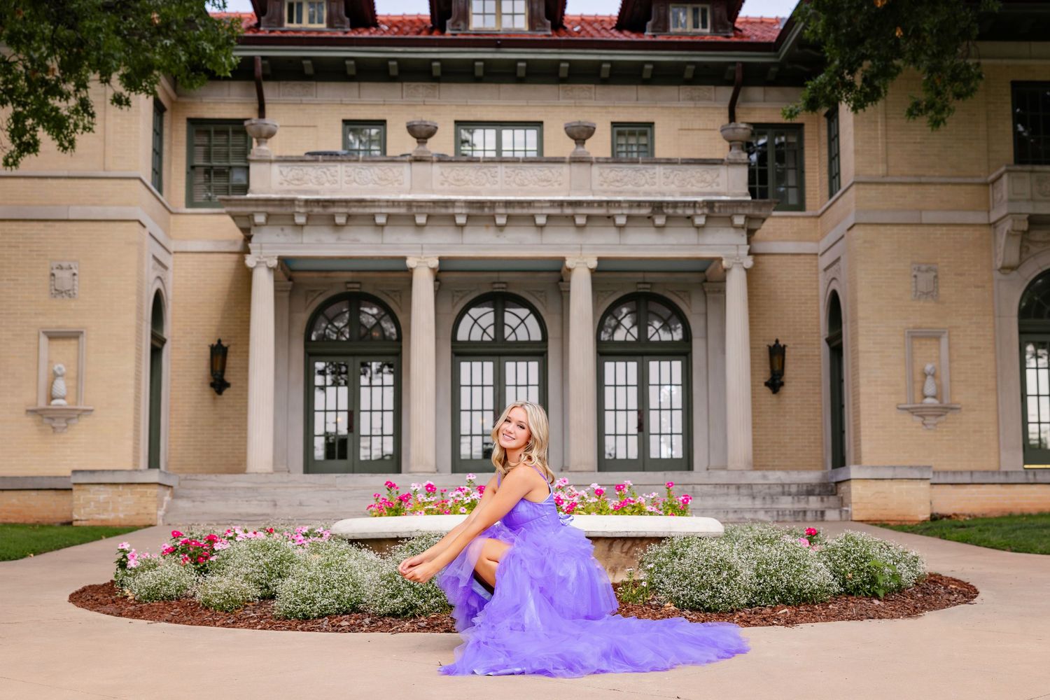 high school senior girl in purple ballgown poses in front of elegant Garden Center mansion gardens in Tulsa, OK .