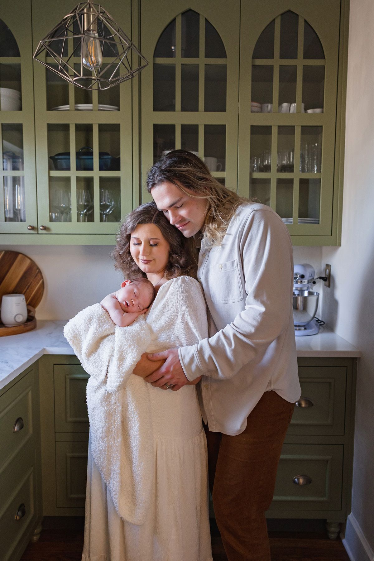 A series of tender moments between two people in a kitchen with sage green cabinets.