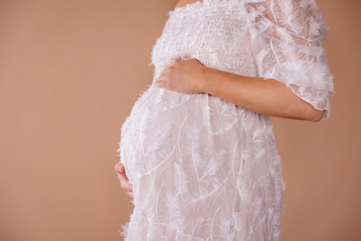 Close-up details of white lace maternity dress with delicate floral patterns.