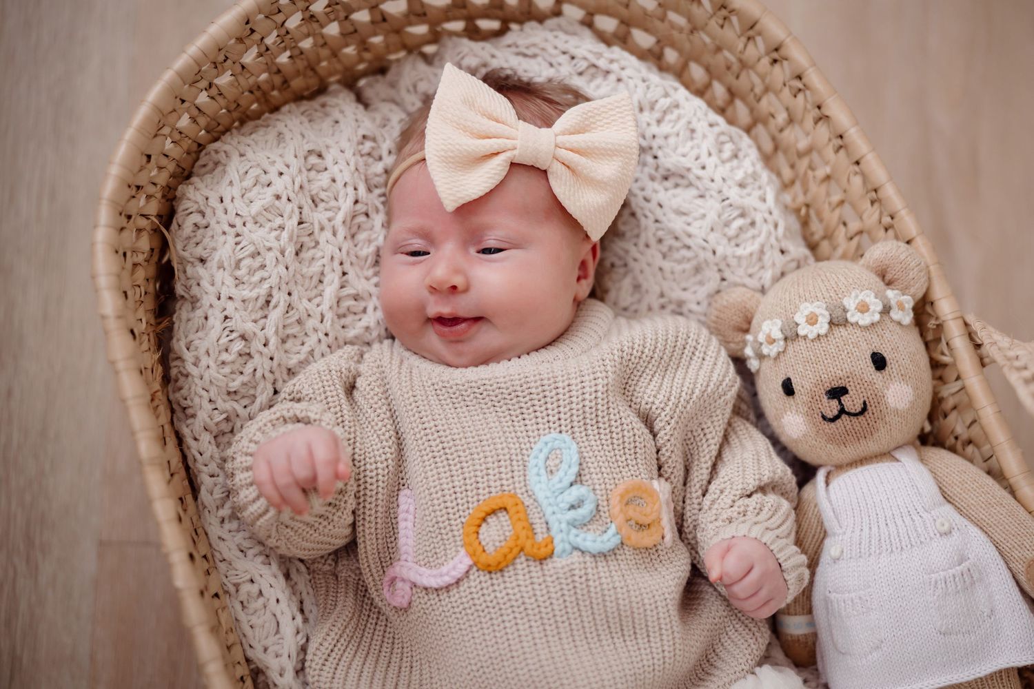 Sleeping newborn photographed with soft knit accessories and pastel decorations in a basket.