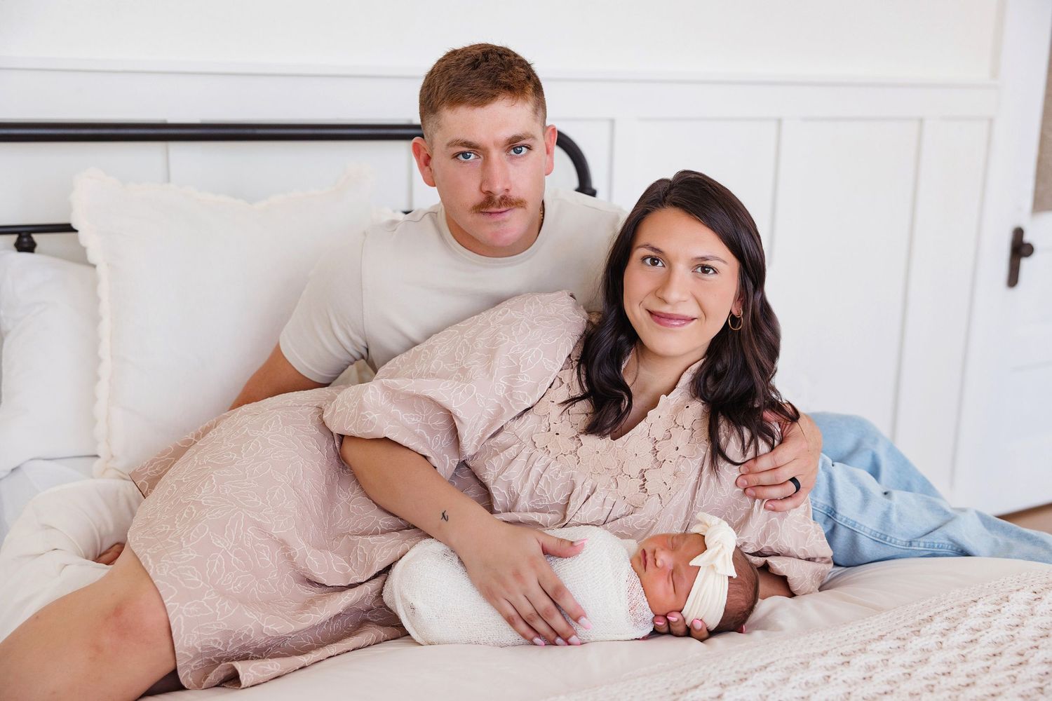 Couple relaxing together on white bedding while holding ultrasound photos.