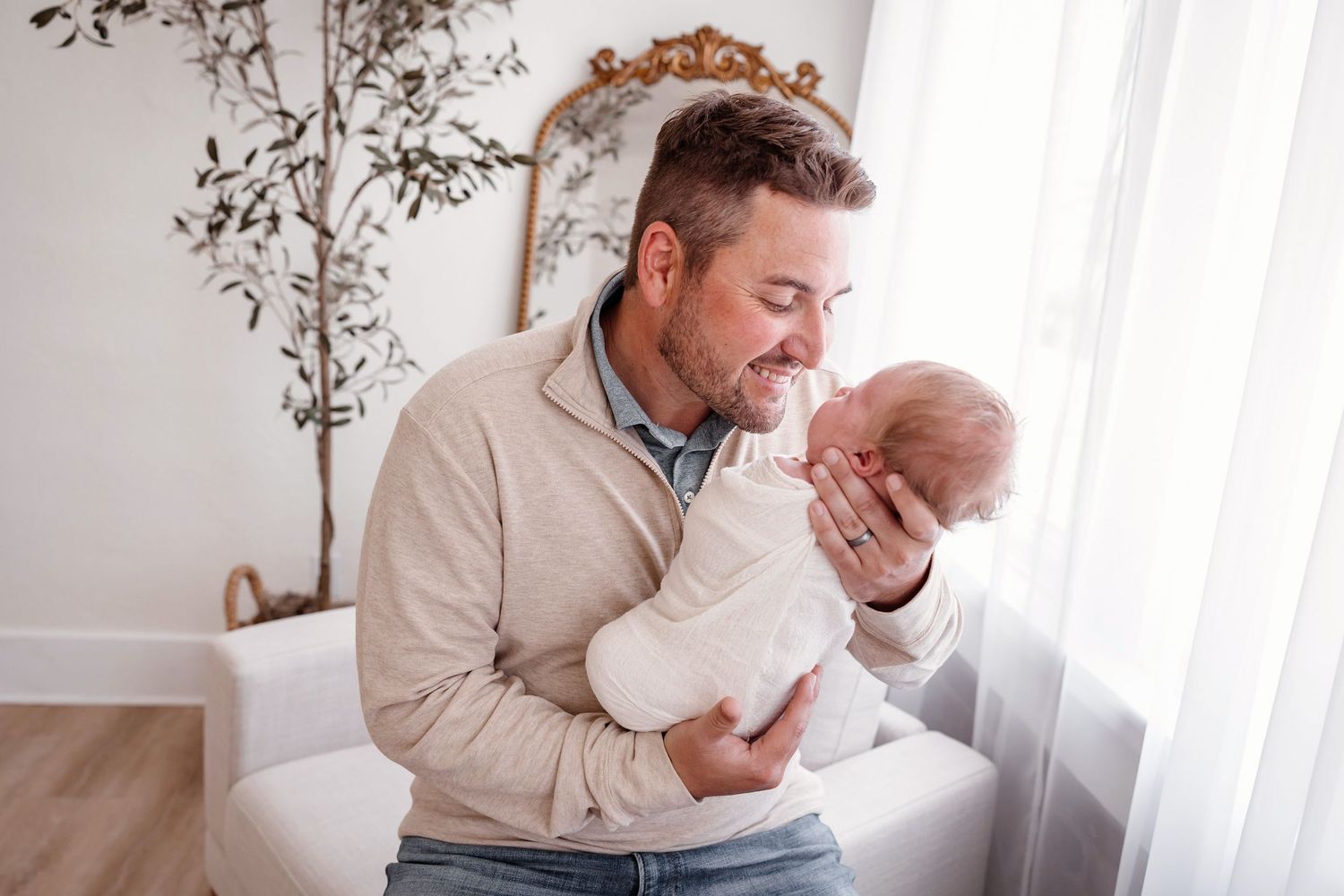 Tender parenting moments captured with father and newborn baby in bright indoor setting.