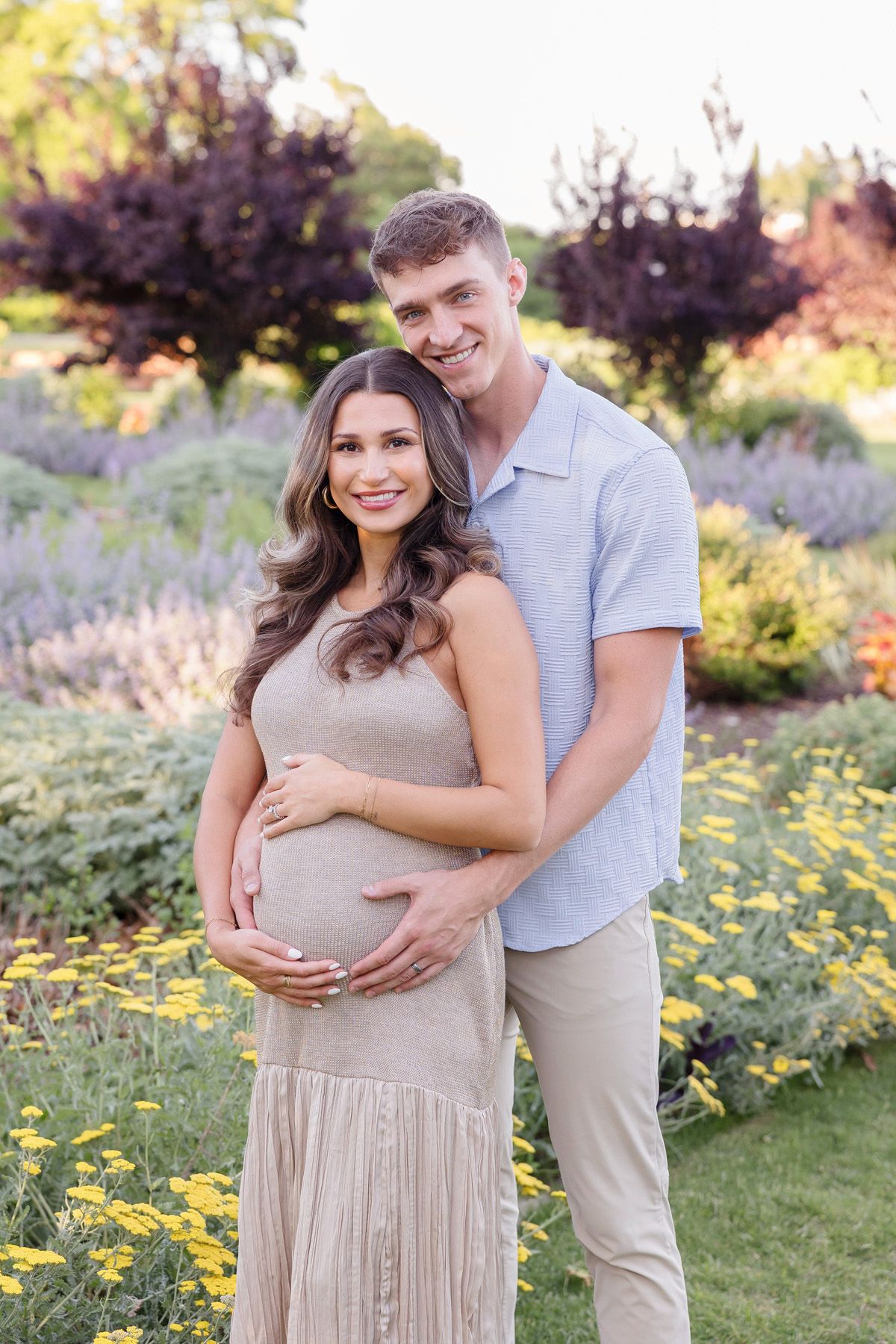 Maternity photos in garden with blooming yellow flowers and couple in neutral tones.