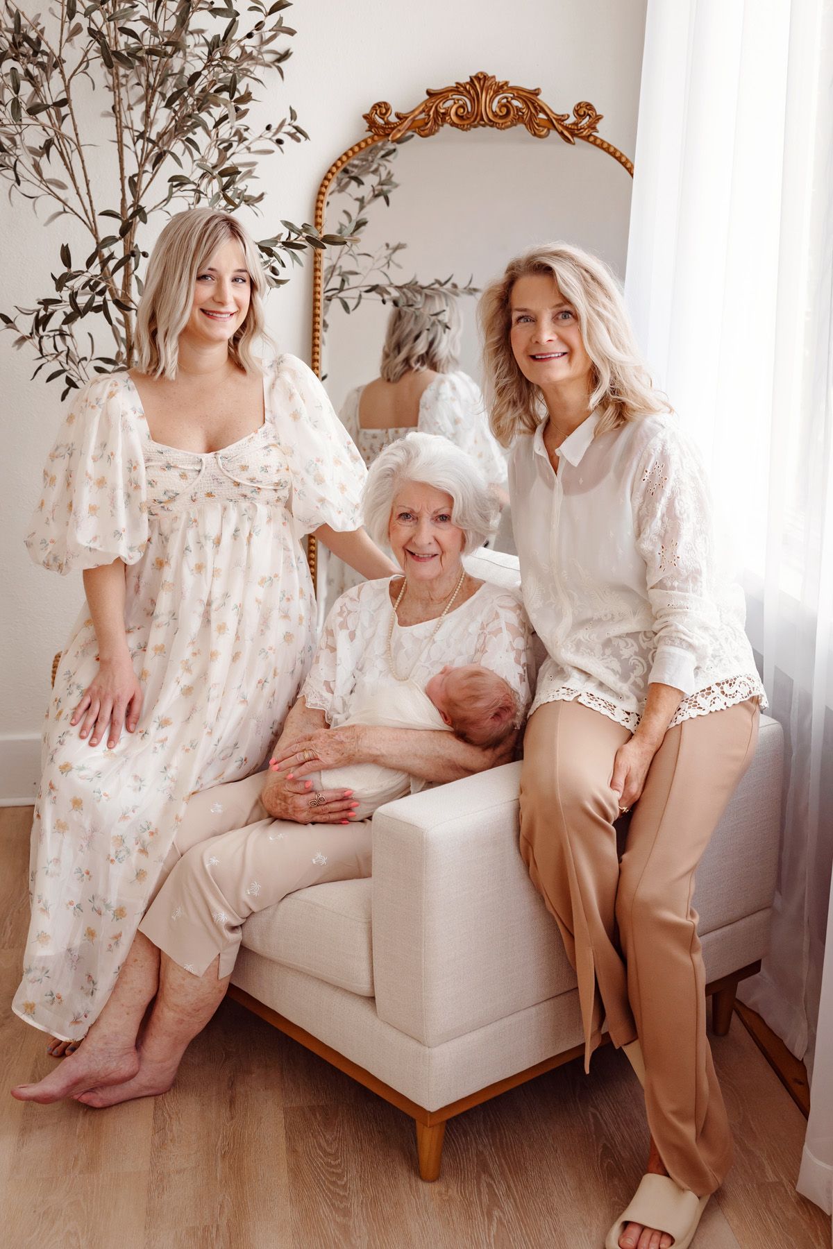 Elegant family portrait session on white furniture with soft floral dresses and neutral tones.