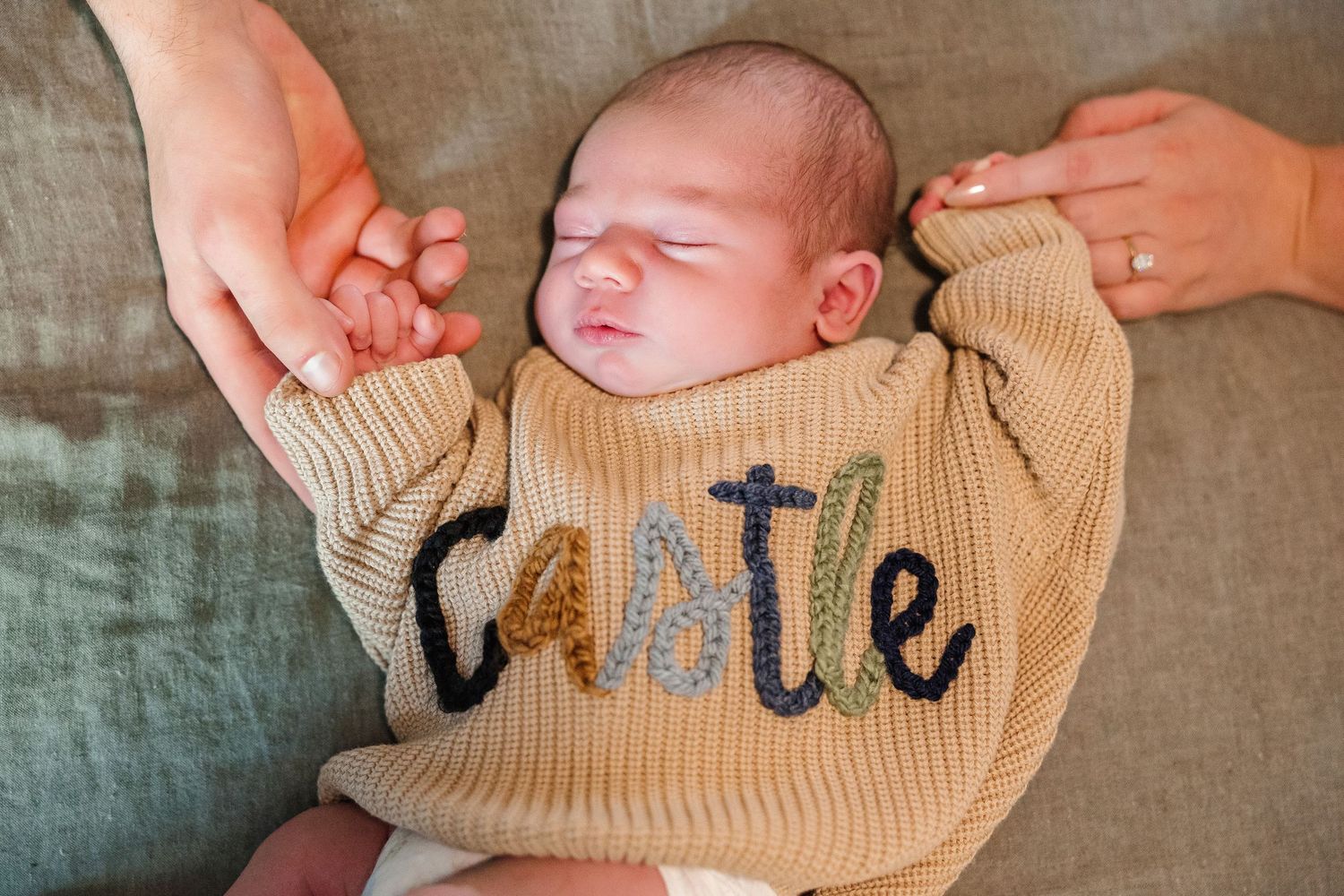 A baby wearing a beige sweater lies on soft fabric with text details.