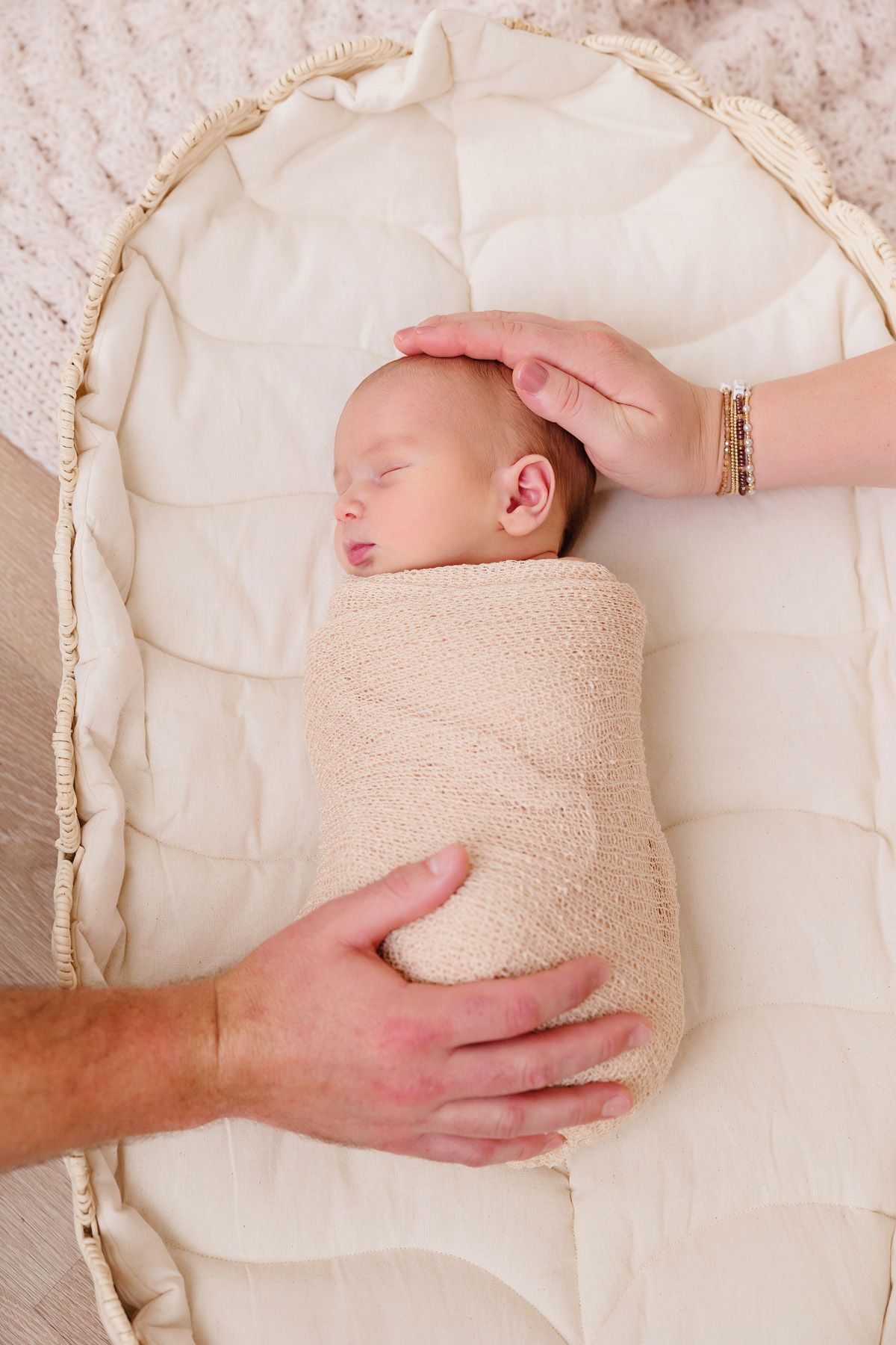 Newborn baby wrapped in beige swaddle on white textured blanket during professional photoshoot.