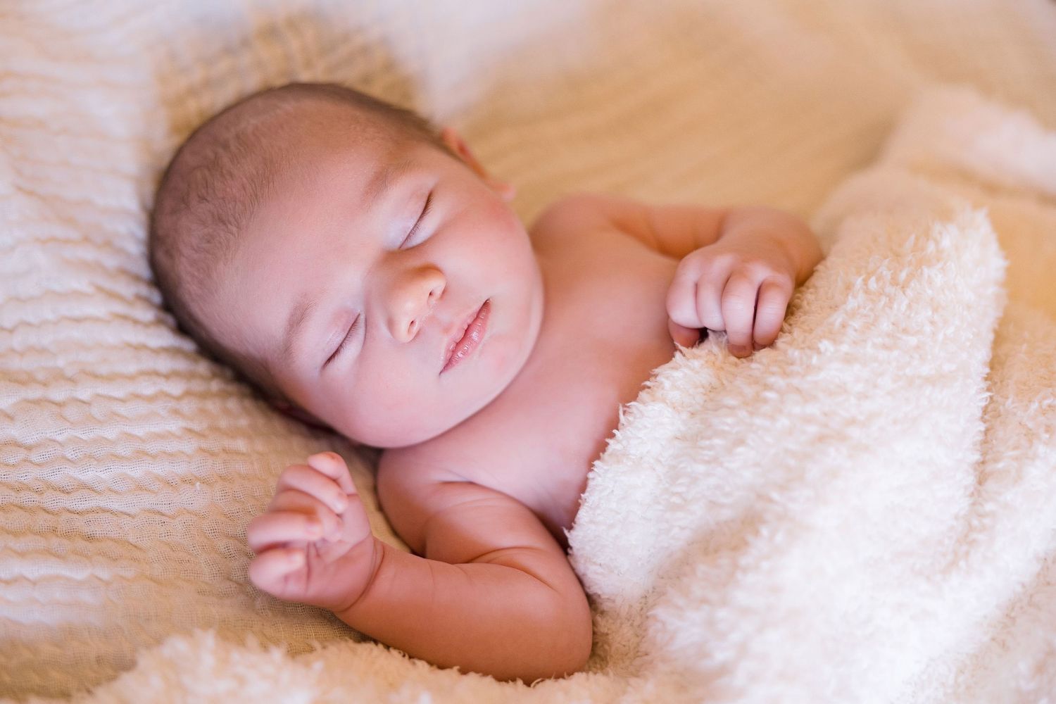 A sleeping newborn baby wrapped in soft cream-colored blankets.