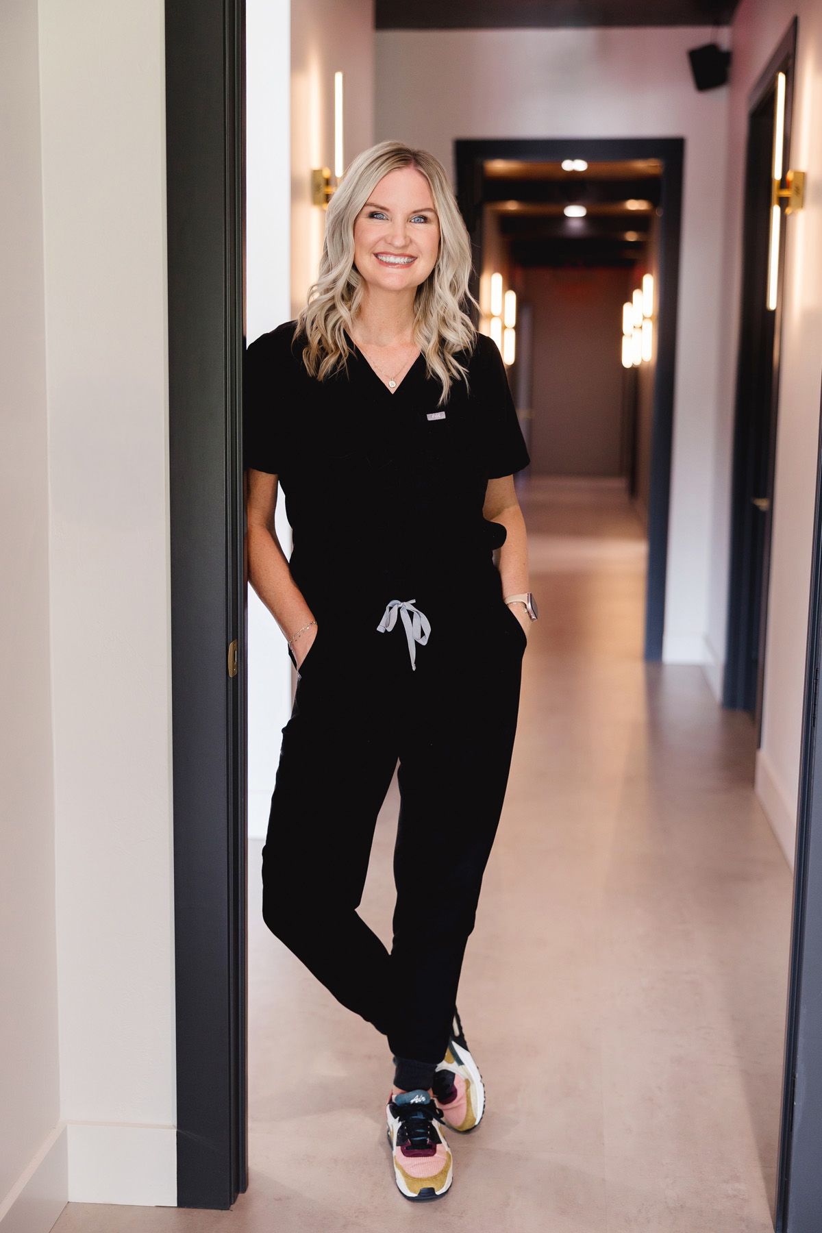 Professional wearing a black outfit walks down a modern hallway with white walls and wooden floors.