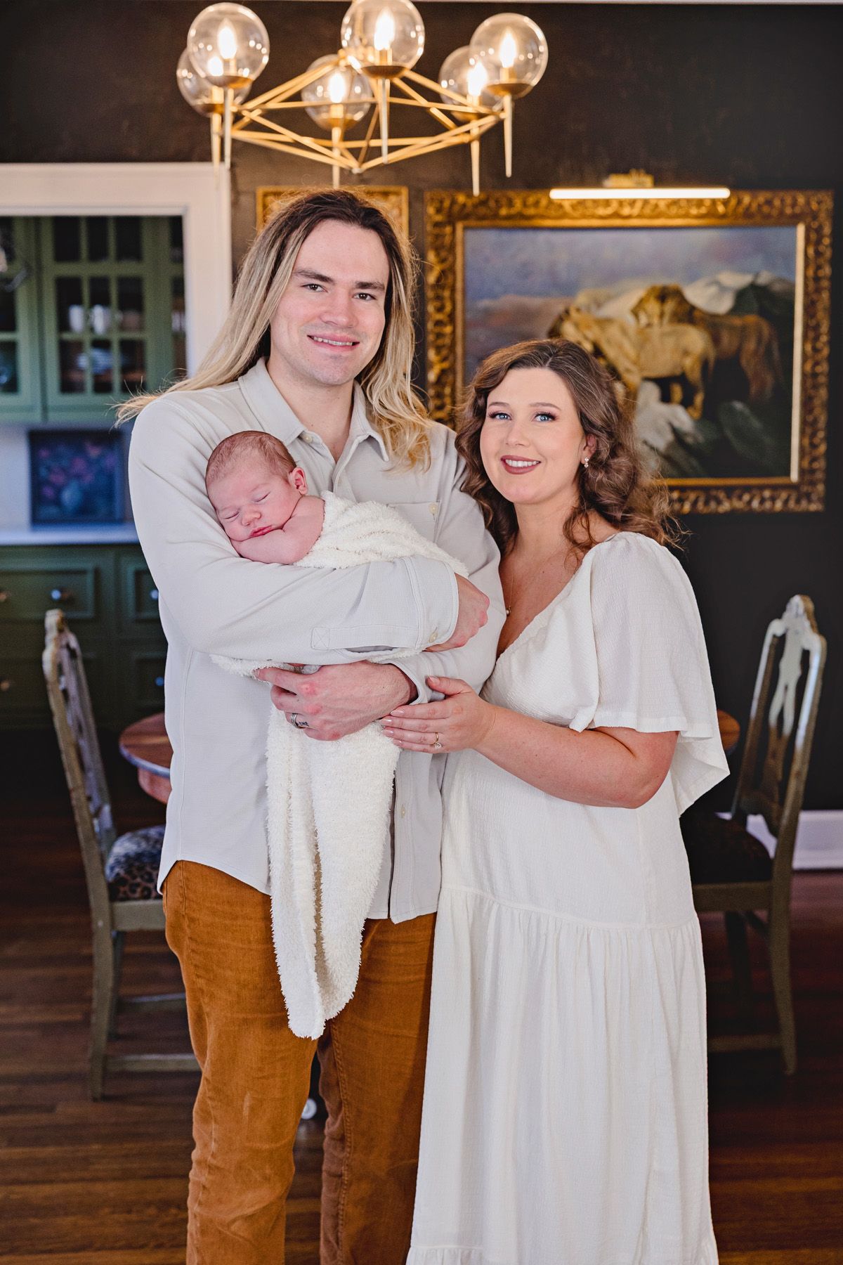 Family portrait in front of an elegant chandelier with parents holding their newborn baby.