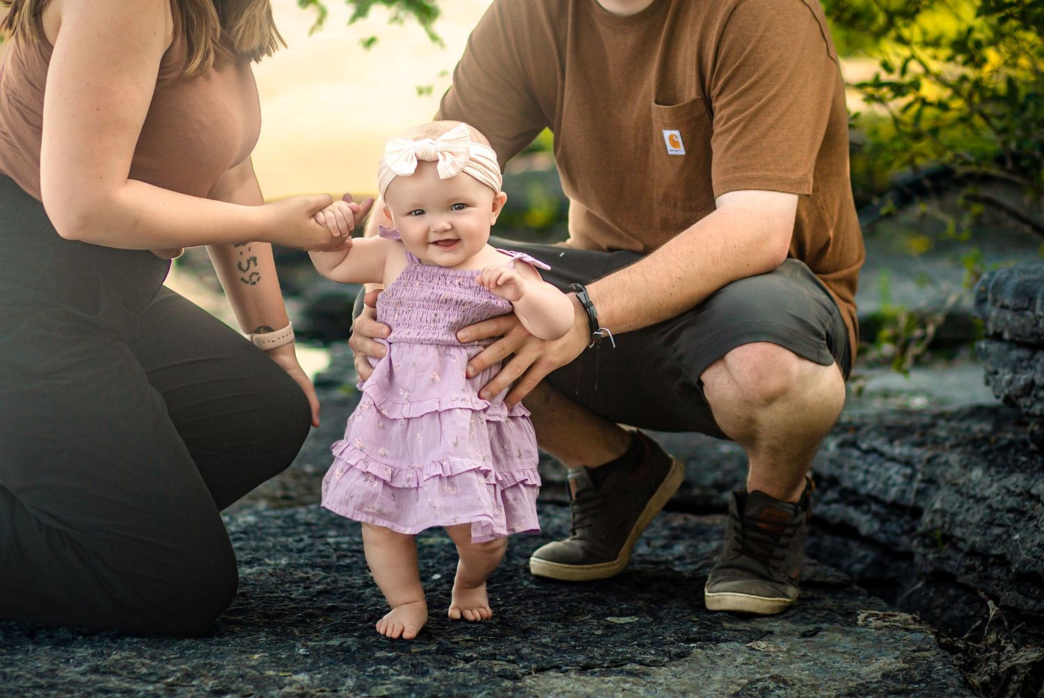 Family photo session with baby girl in a dress, standing while supported by her proud parents, photo session with Kingston photographer.