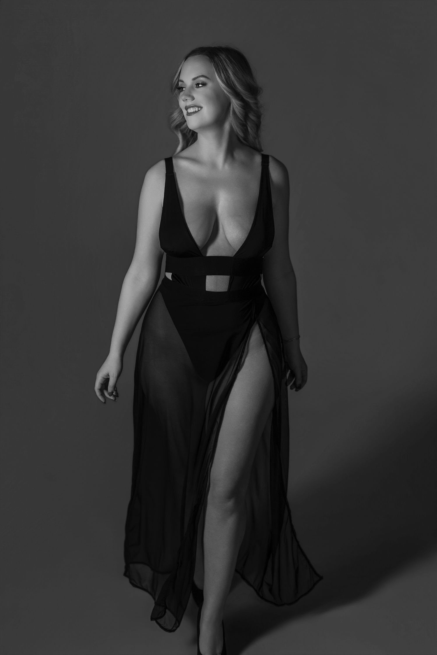 Black and white fashion portrait of a woman in an elegant flowing dress with high slit posing against dark background in maryland.